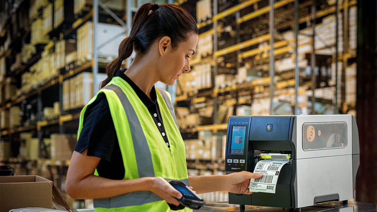 A female warehouse worker grabs a label off an industrial printer