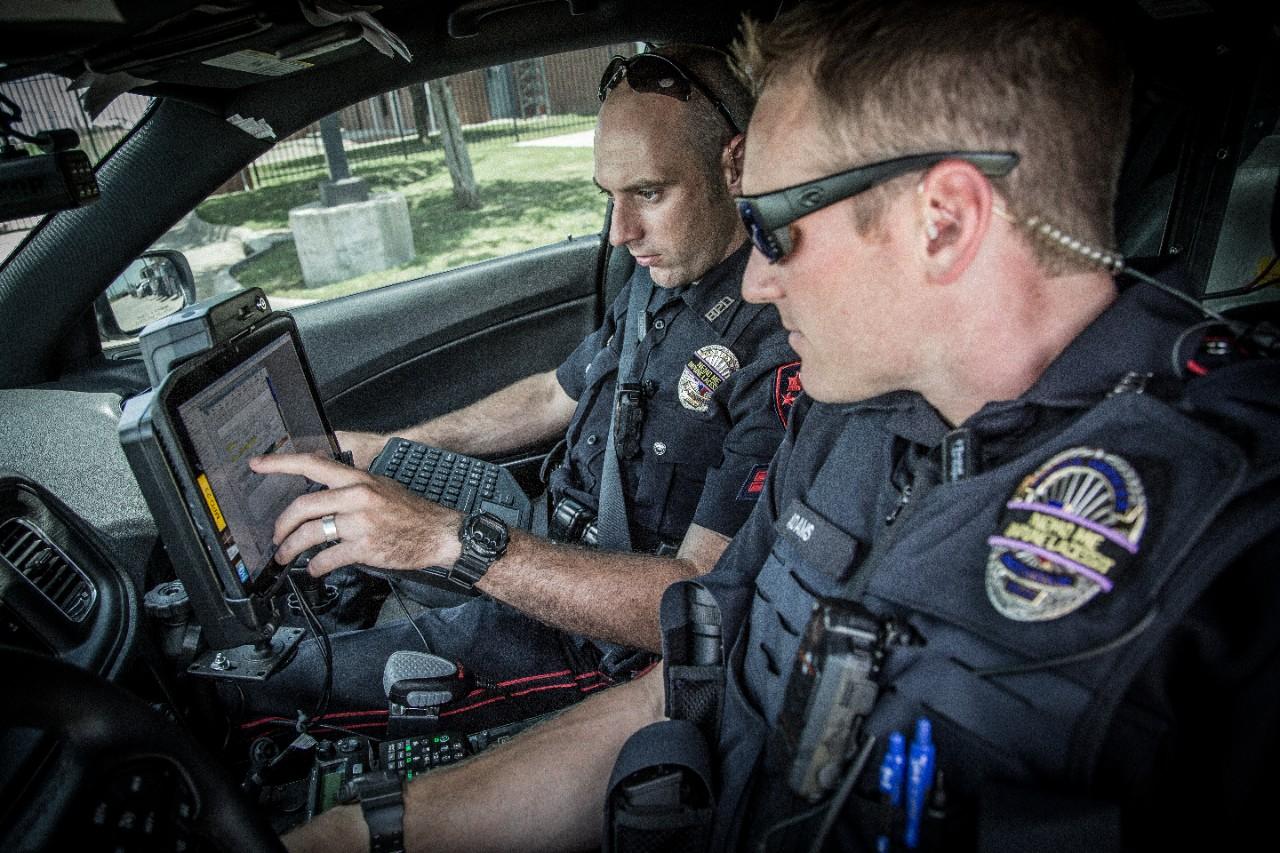 Two police officers look at a rugged tablet mounted in their vehicle for guidance en-route to a call.