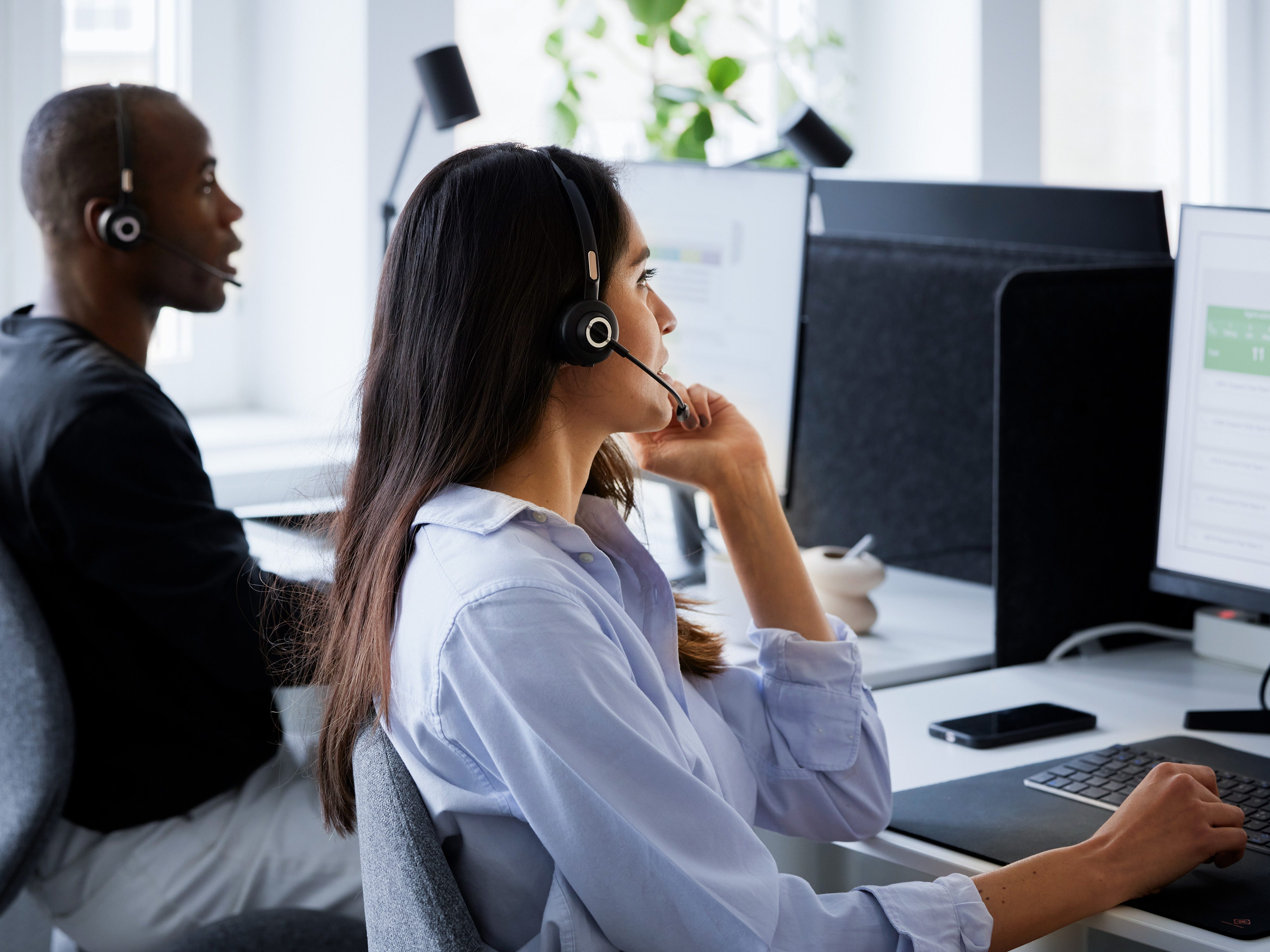 Two call center agents talking with customers at their workstations.