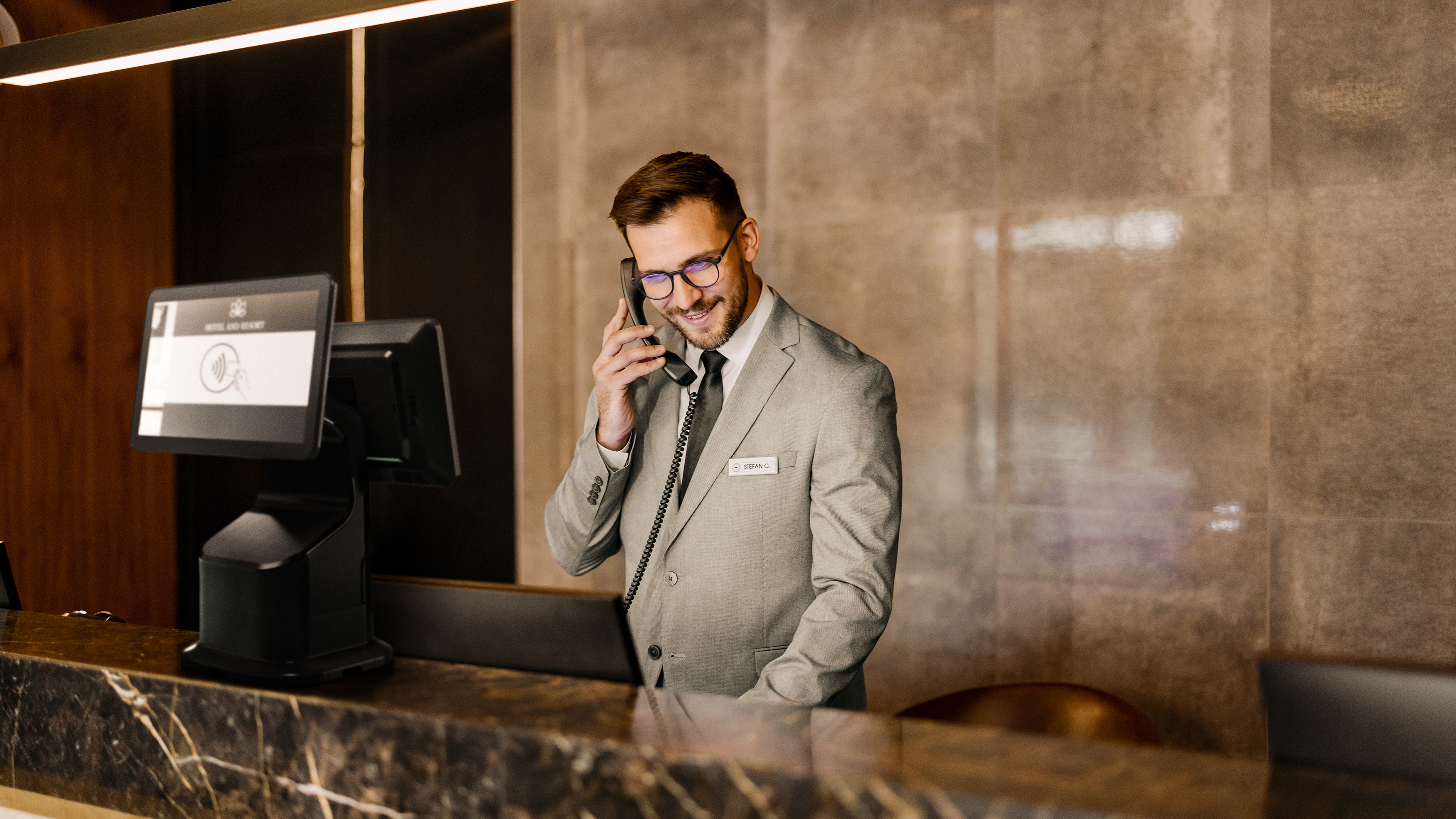 Hotel desk attendant using a phone and a Zebra Interactive Kiosk.