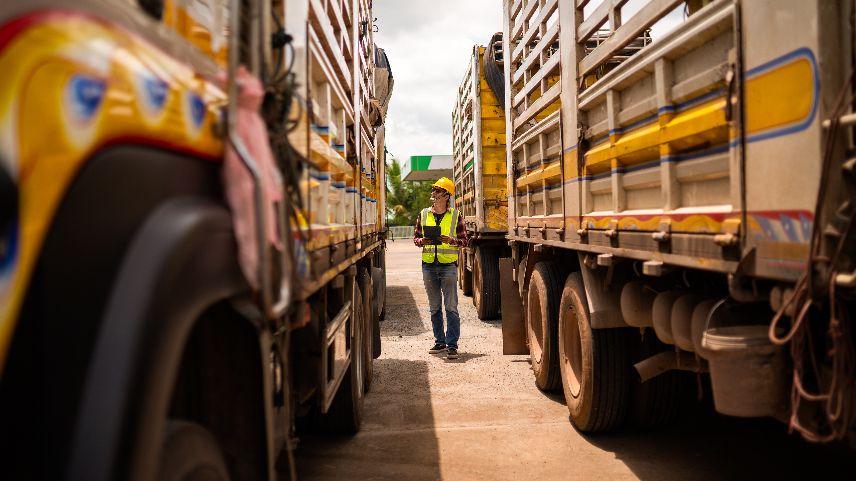 Logistics worker using a tablet in between two delivery trucks. 