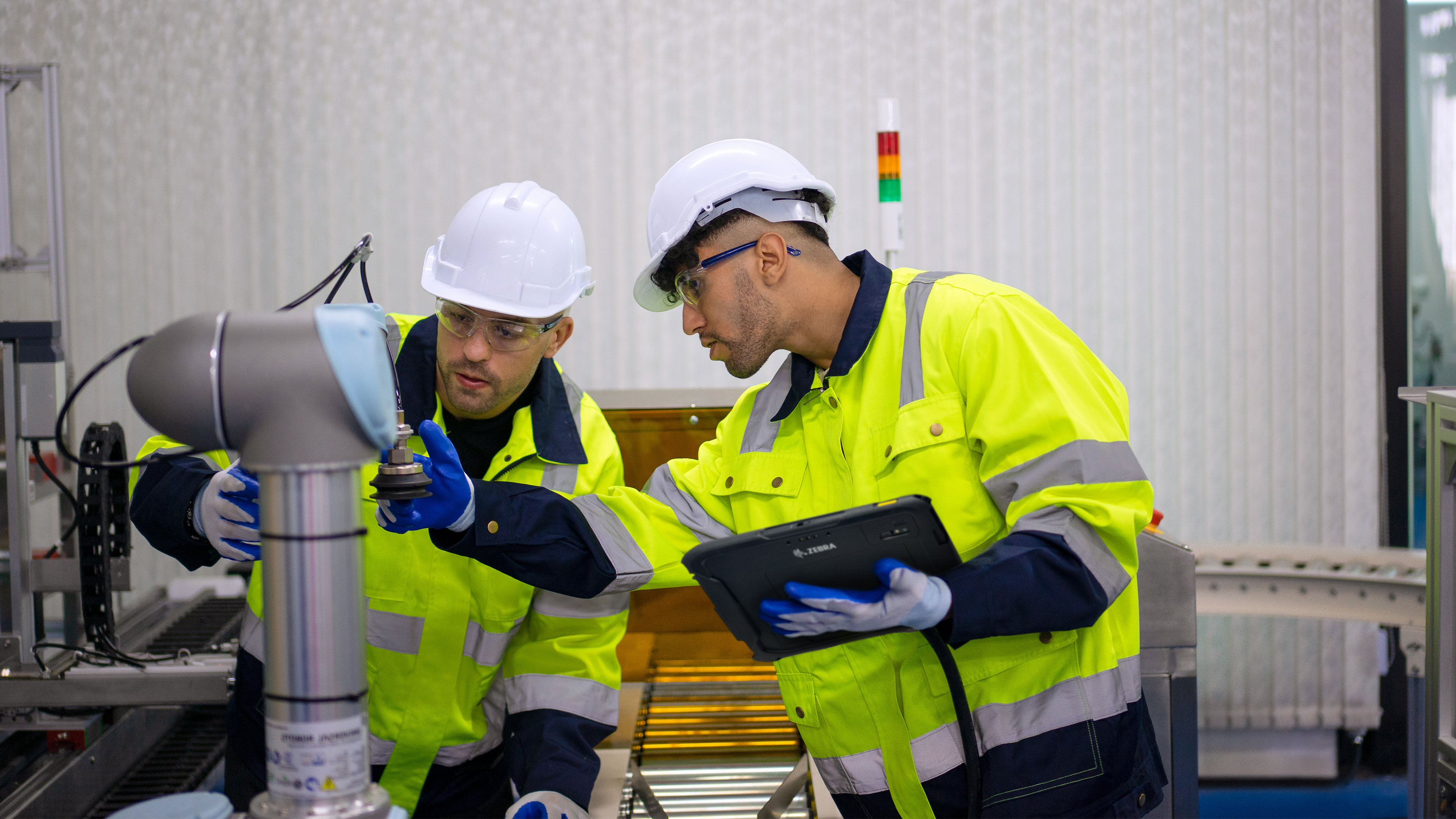 Two engineers configuring an industrial robotic arm using a Zebra tablet.
