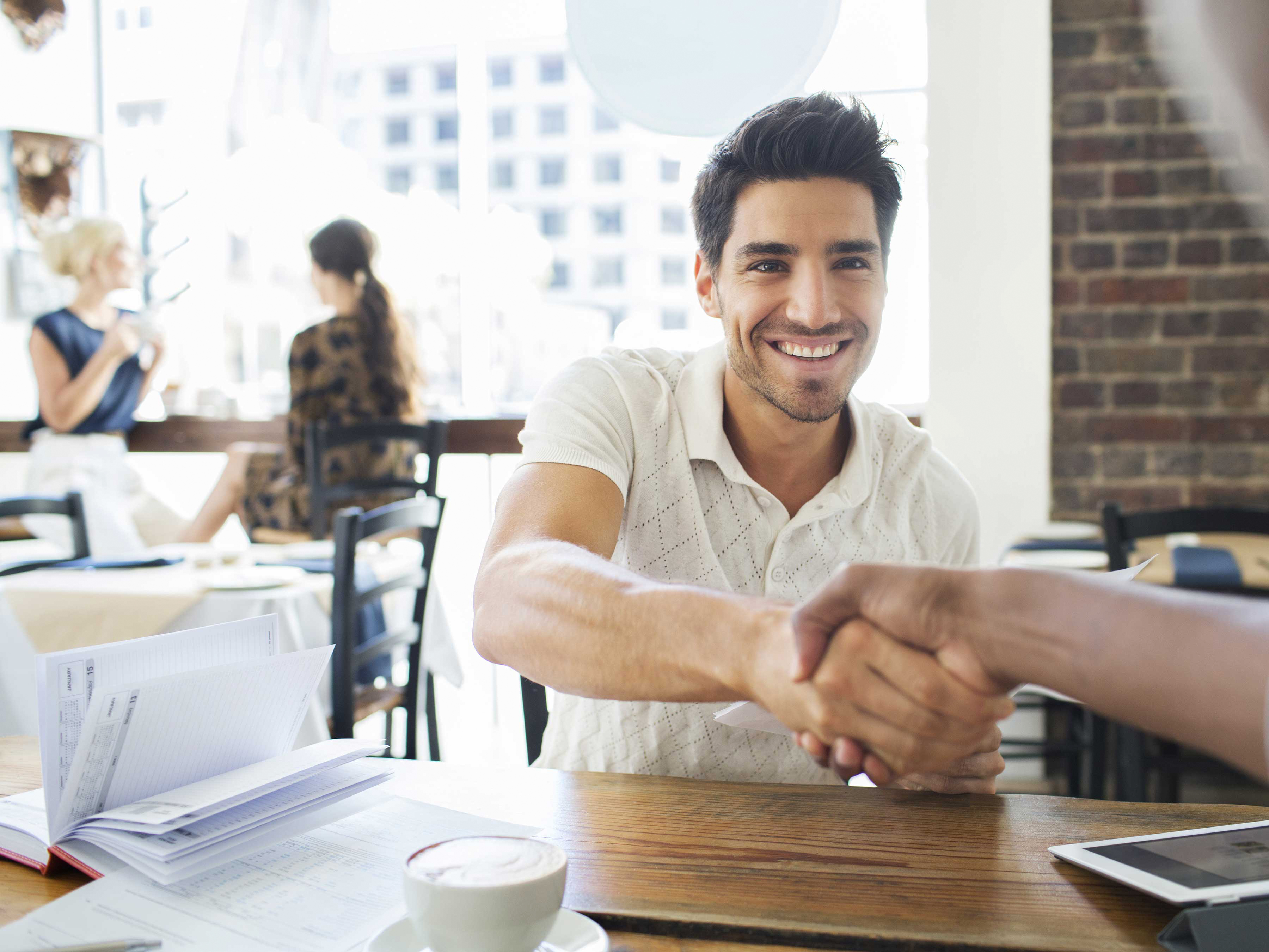Two colleagues shaking hands in a cafe. 