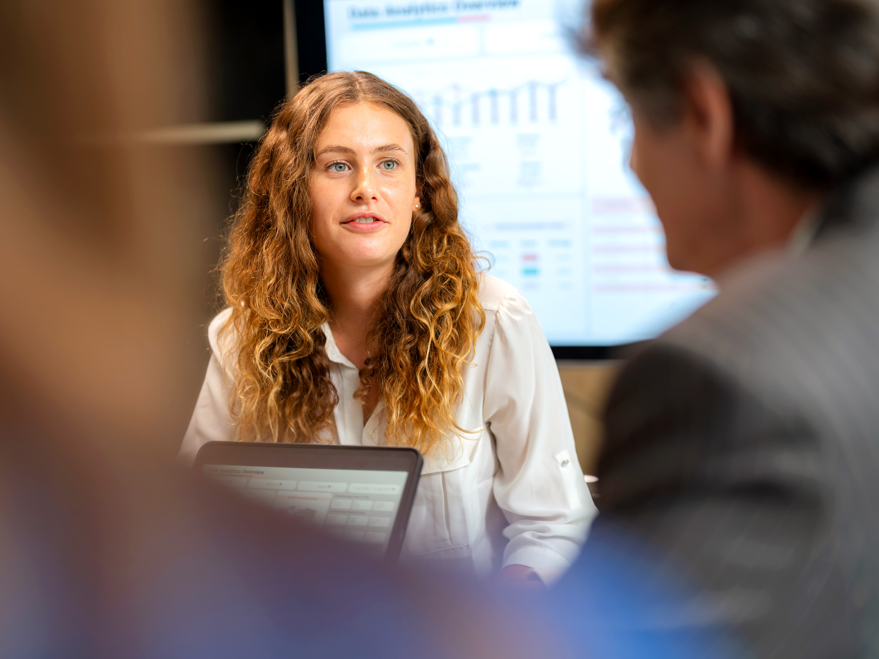 Woman leading a meeting with a laptop on hands and a chart on screen in the background