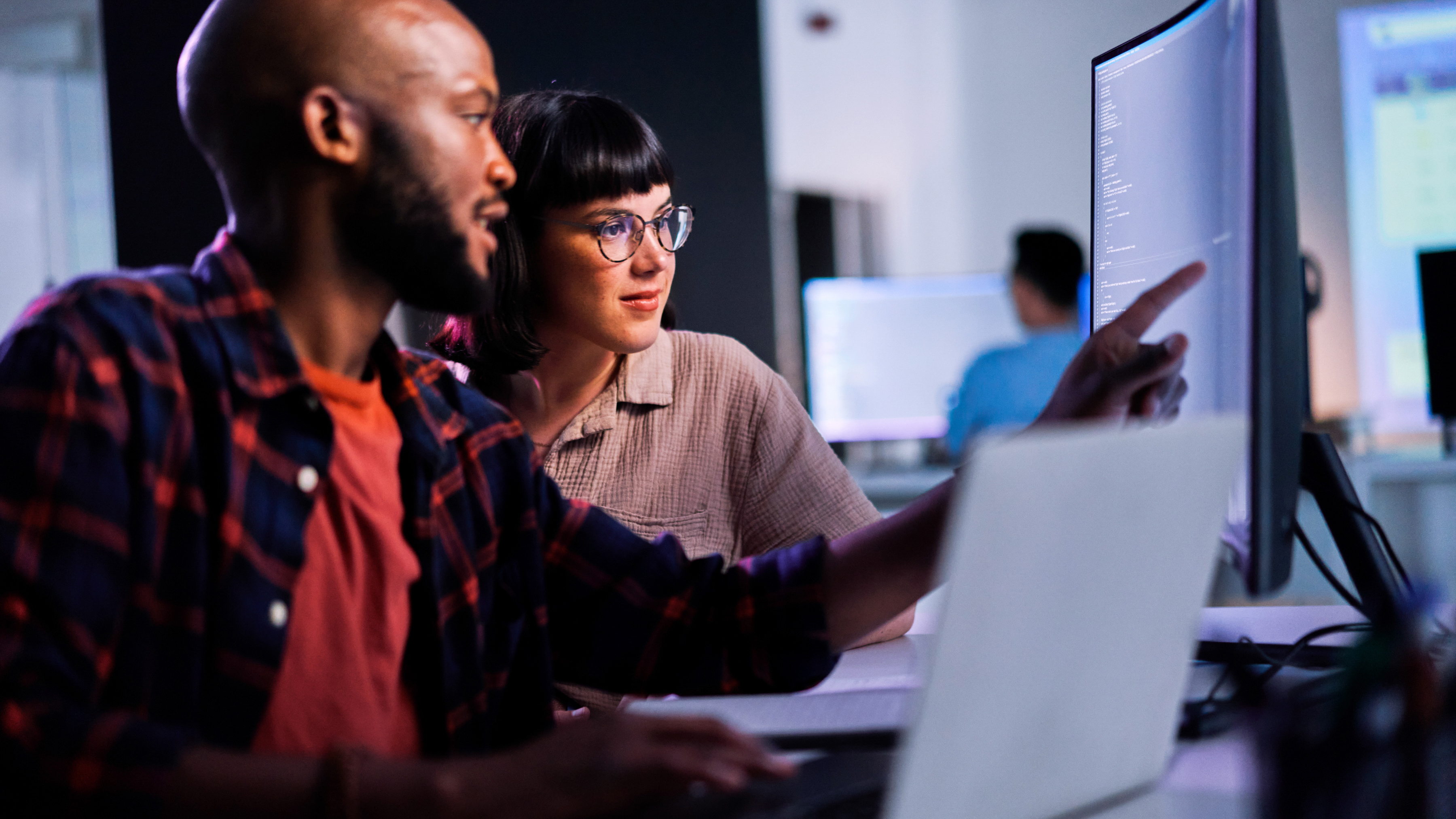Two employees collaborating in front of a large desktop monitor at work.