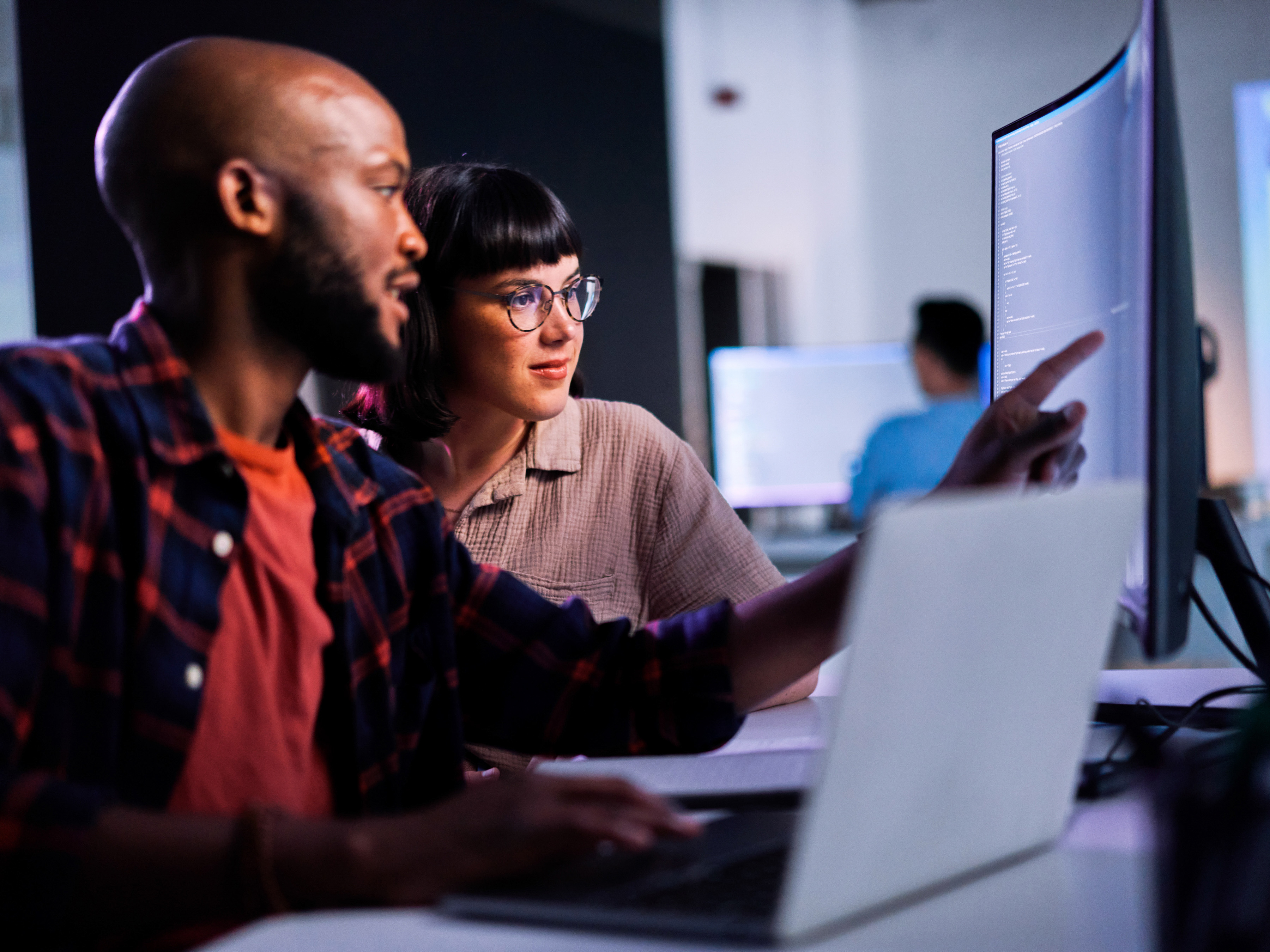 Two employees collaborating in front of a large desktop monitor at work.