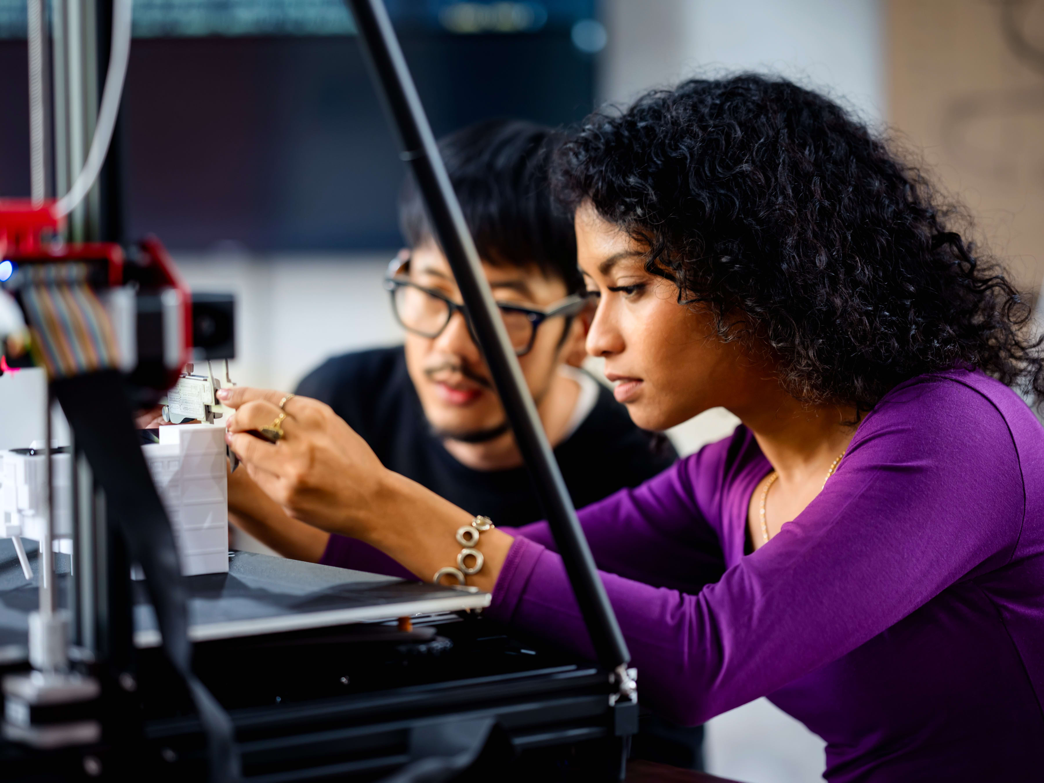 Two coworkers using a 3D printer to build a product together.