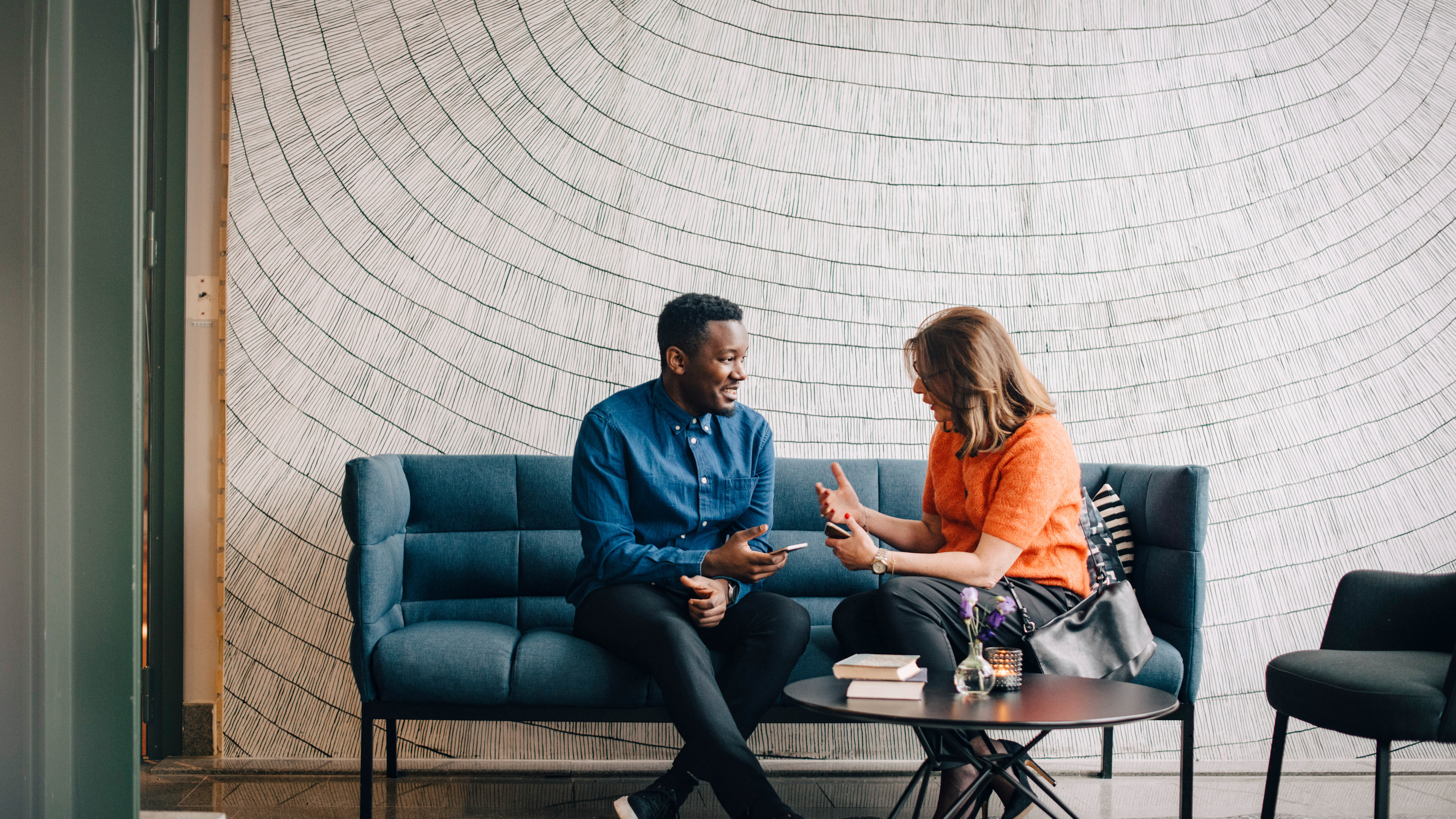 Two colleagues are having a conversation in an office lobby while holding their mobile computers.
