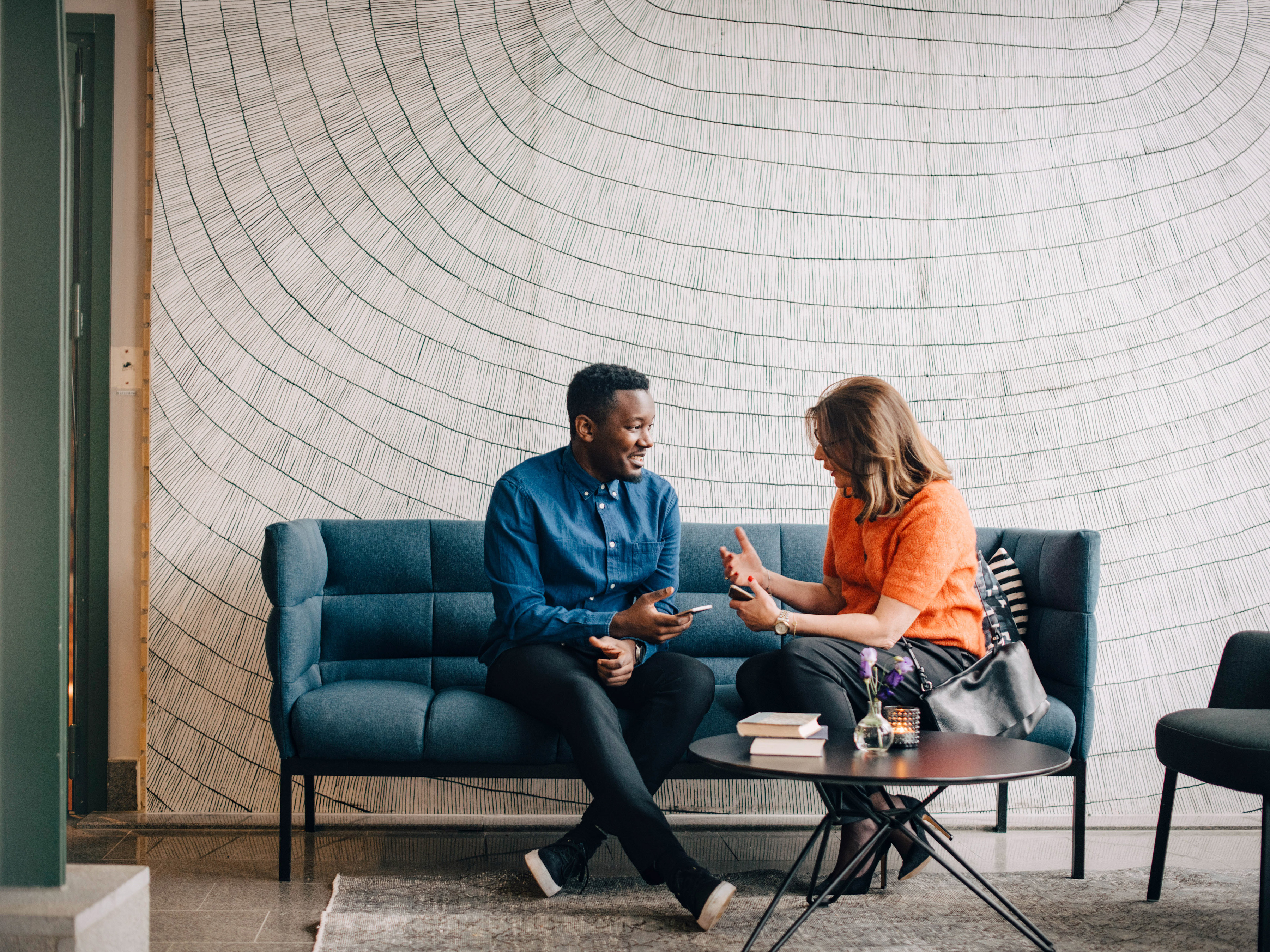 Two colleagues are having a conversation in an office lobby while holding their mobile computers.