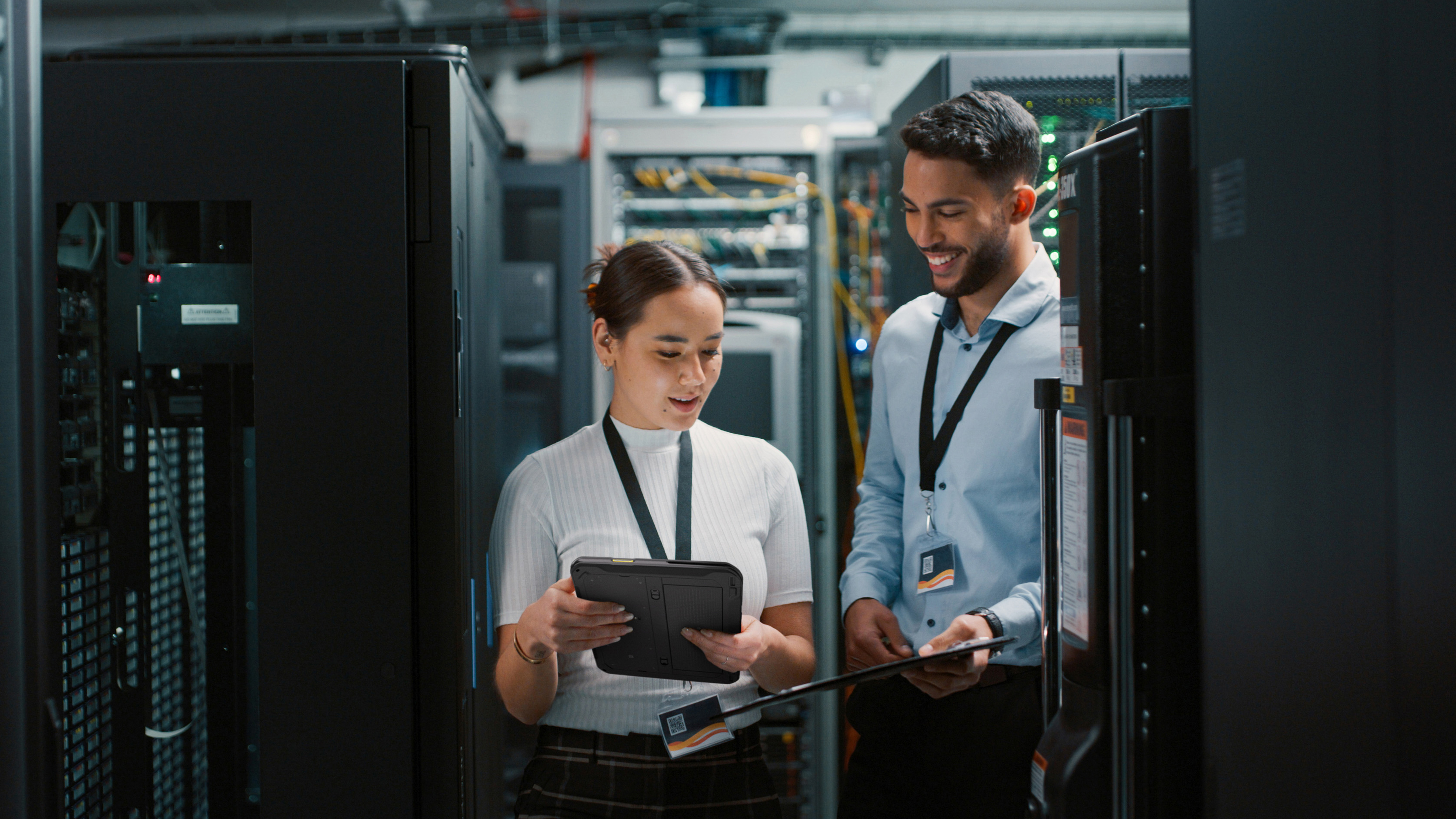 Two coworkers reviewing their Zebra tablet and handheld mobile computer inside of a server room.