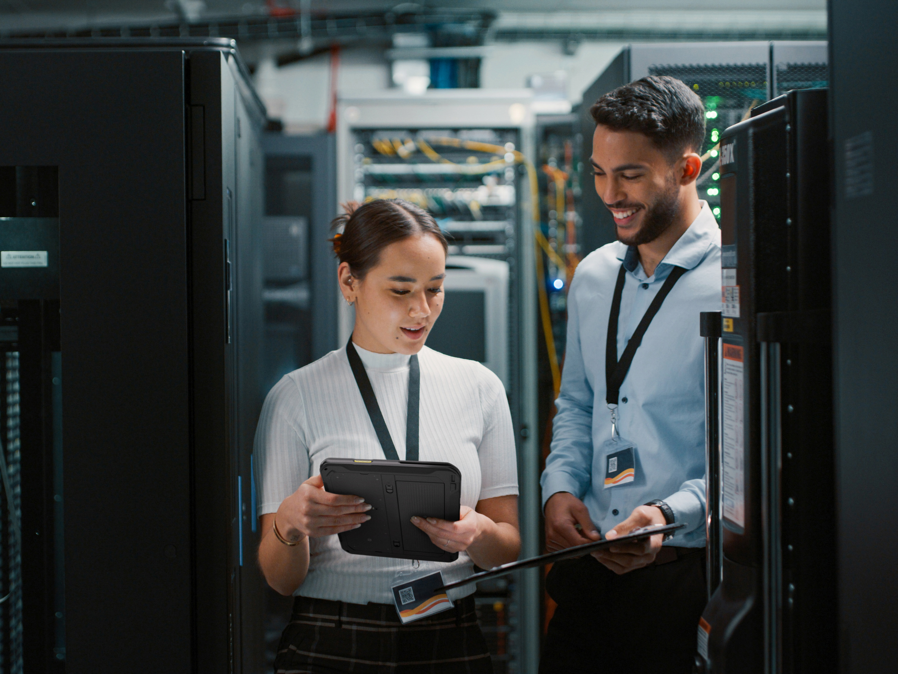 Two coworkers reviewing their Zebra tablet and handheld mobile computer inside of a server room.