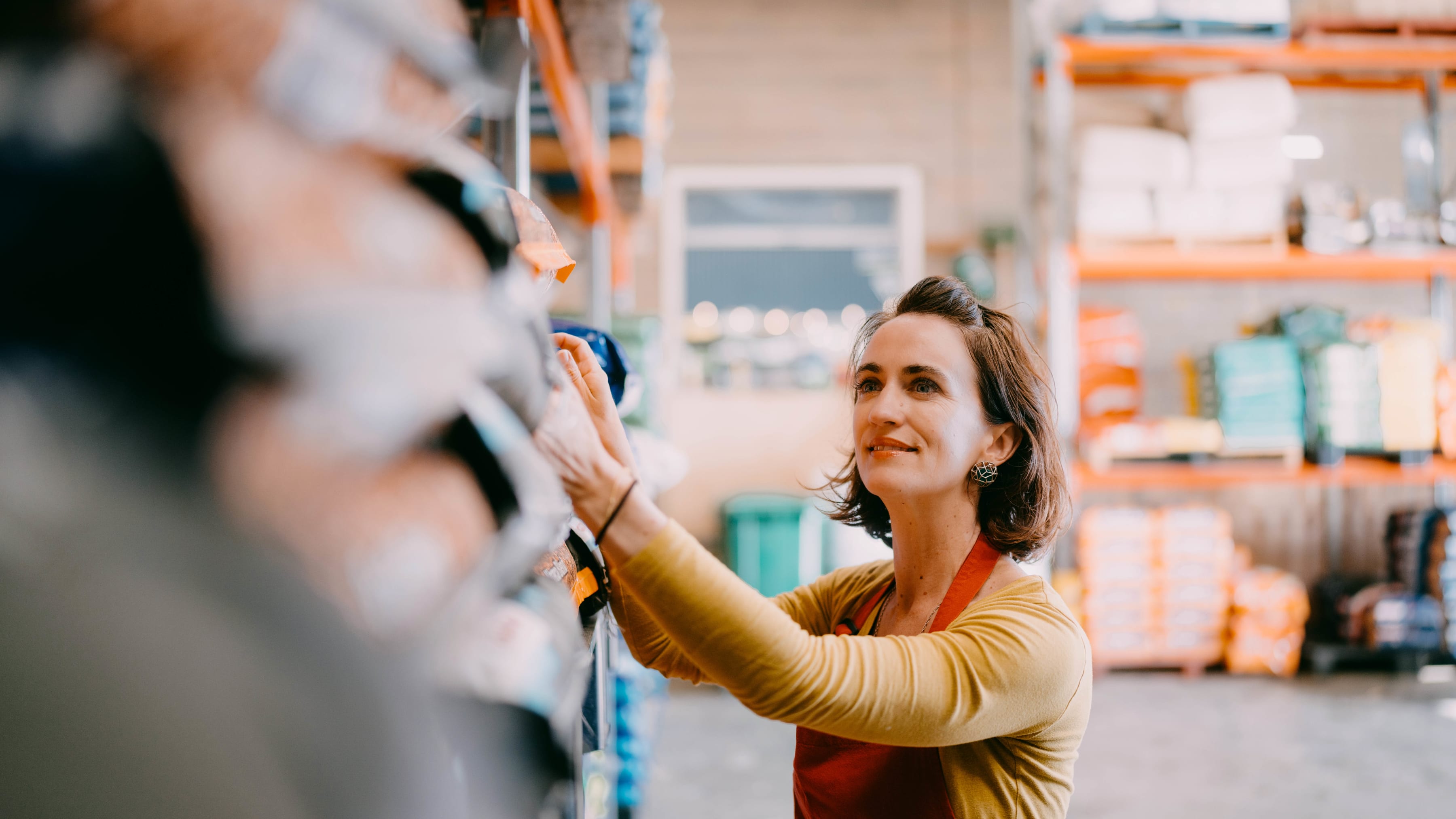 An employee is reaching for an item on a shelf at the garden department in a box store.