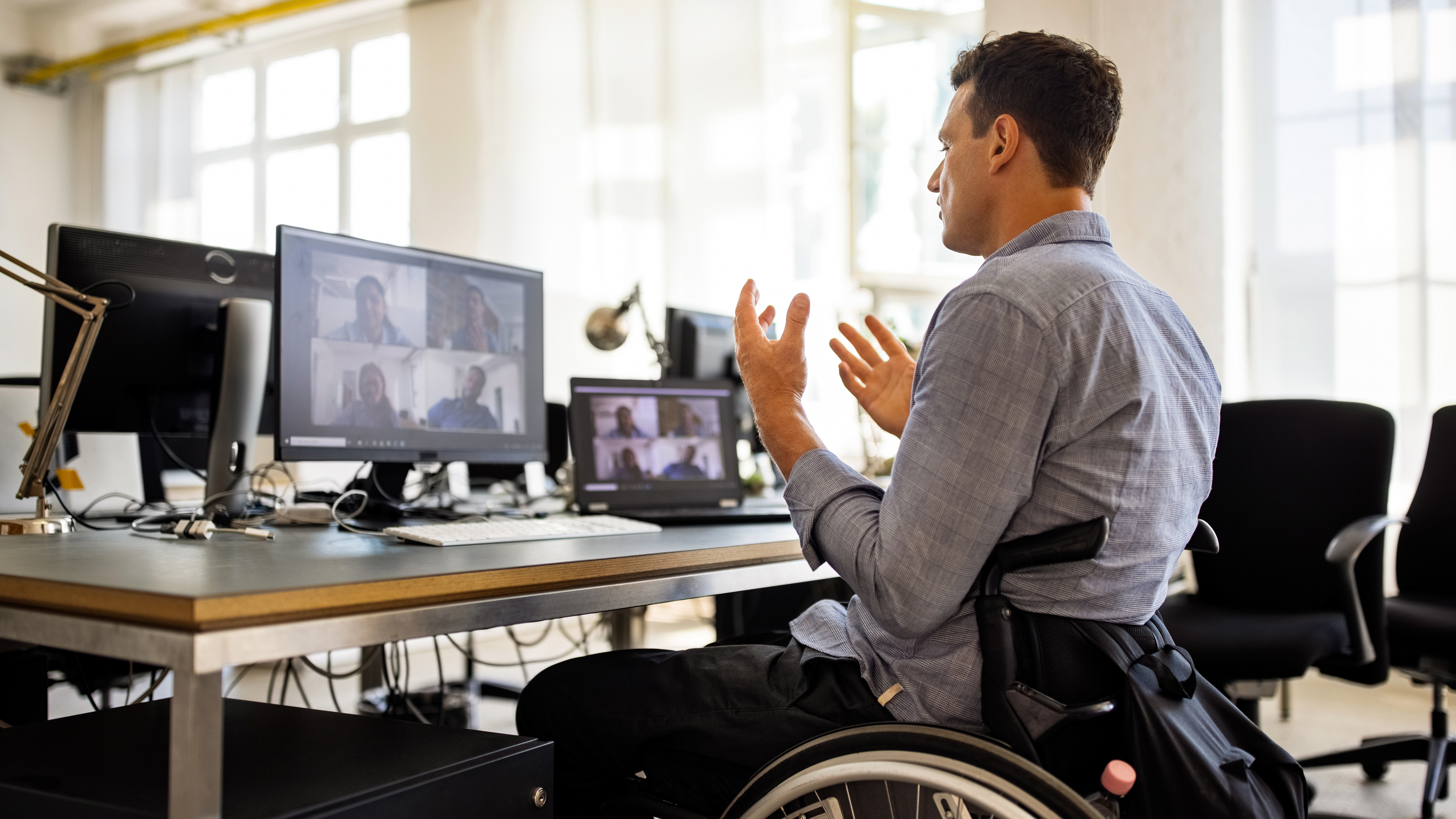Wheelchair bound employee at an office workstation participating in a video conference call.