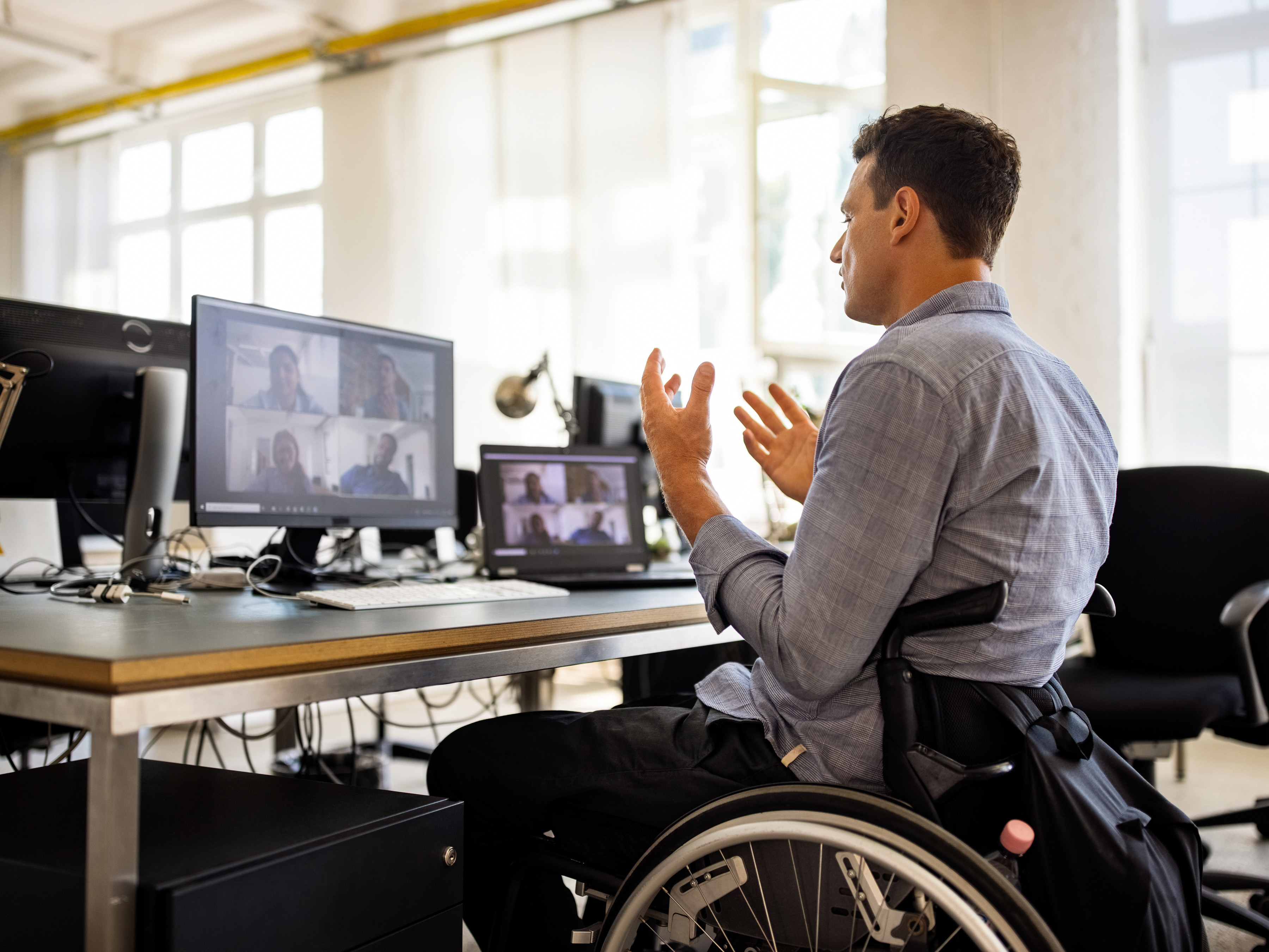 Wheelchair bound employee at an office workstation participating in a video conference call.