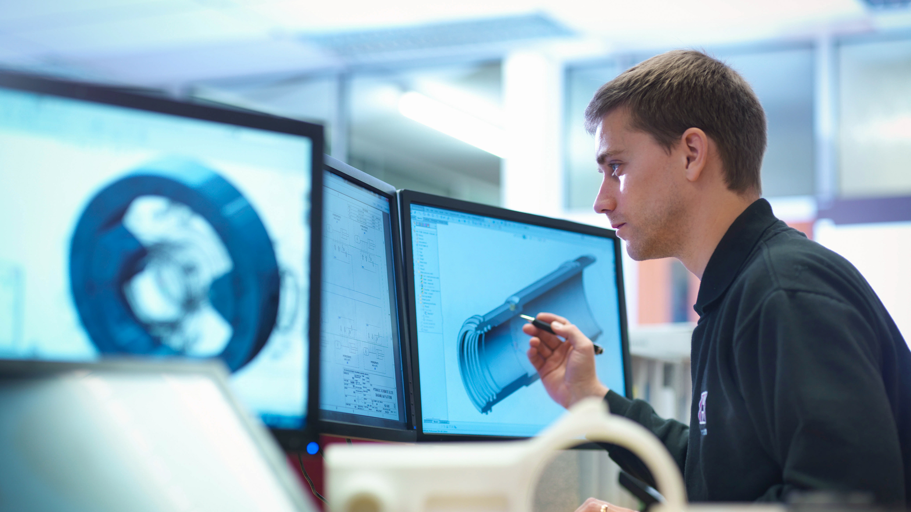 An employee working at a desk and reviewing engineering designs and technical 3D models.