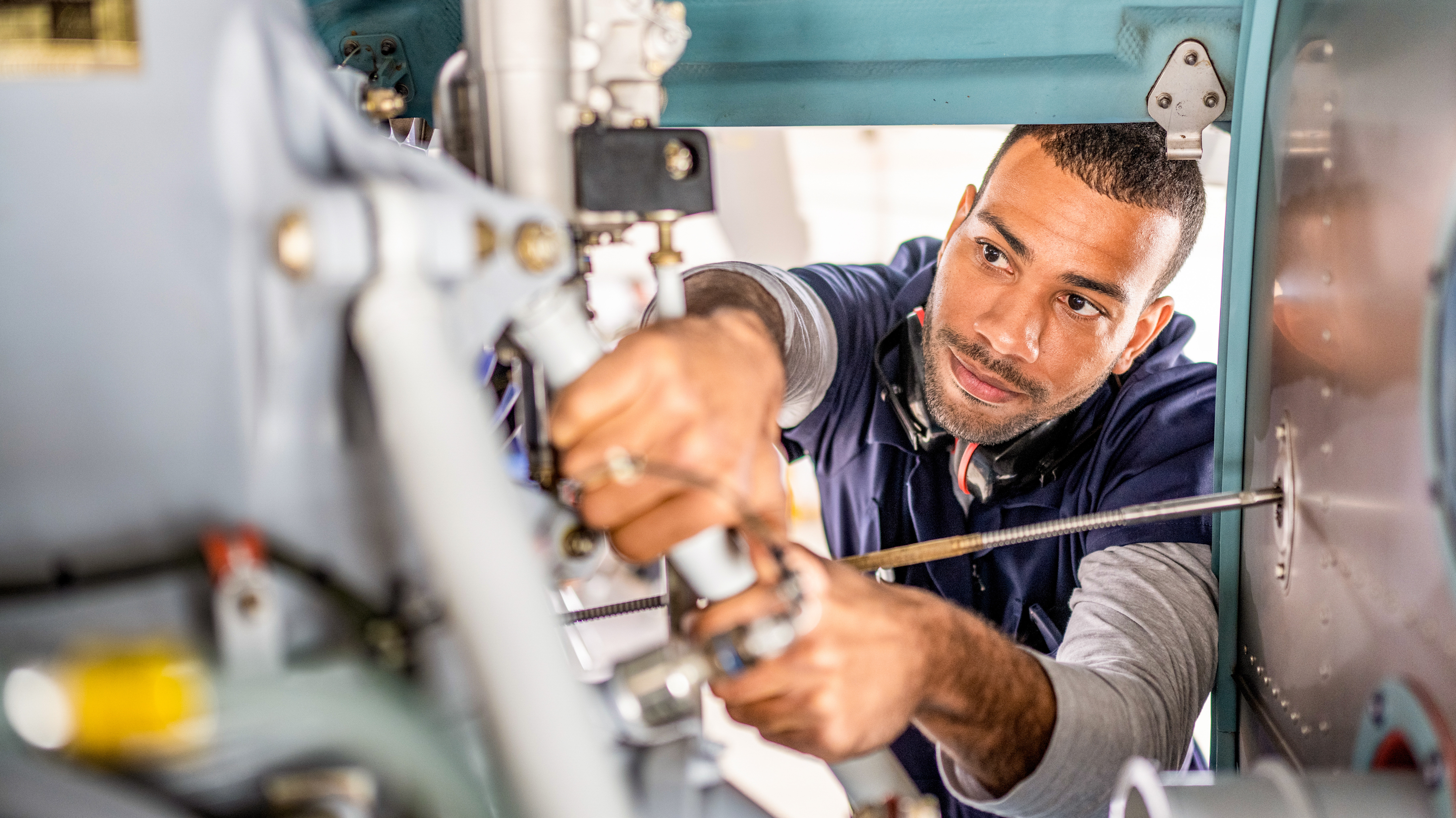 A mechanic is working on machinery, focusing intently on adjusting a component.
