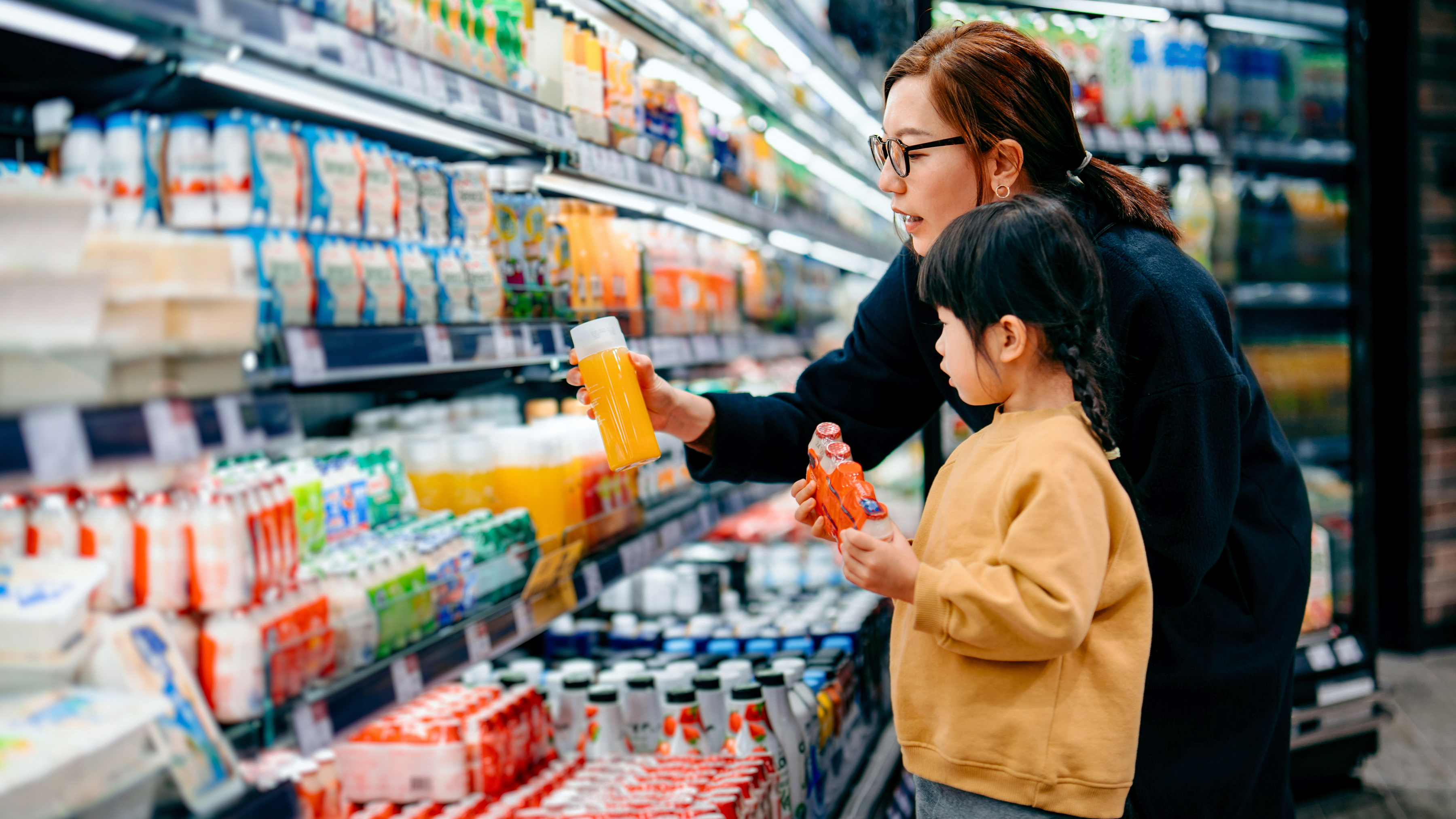 A parent and a child are shopping for beverages in front of a refrigerated section in a grocery store.