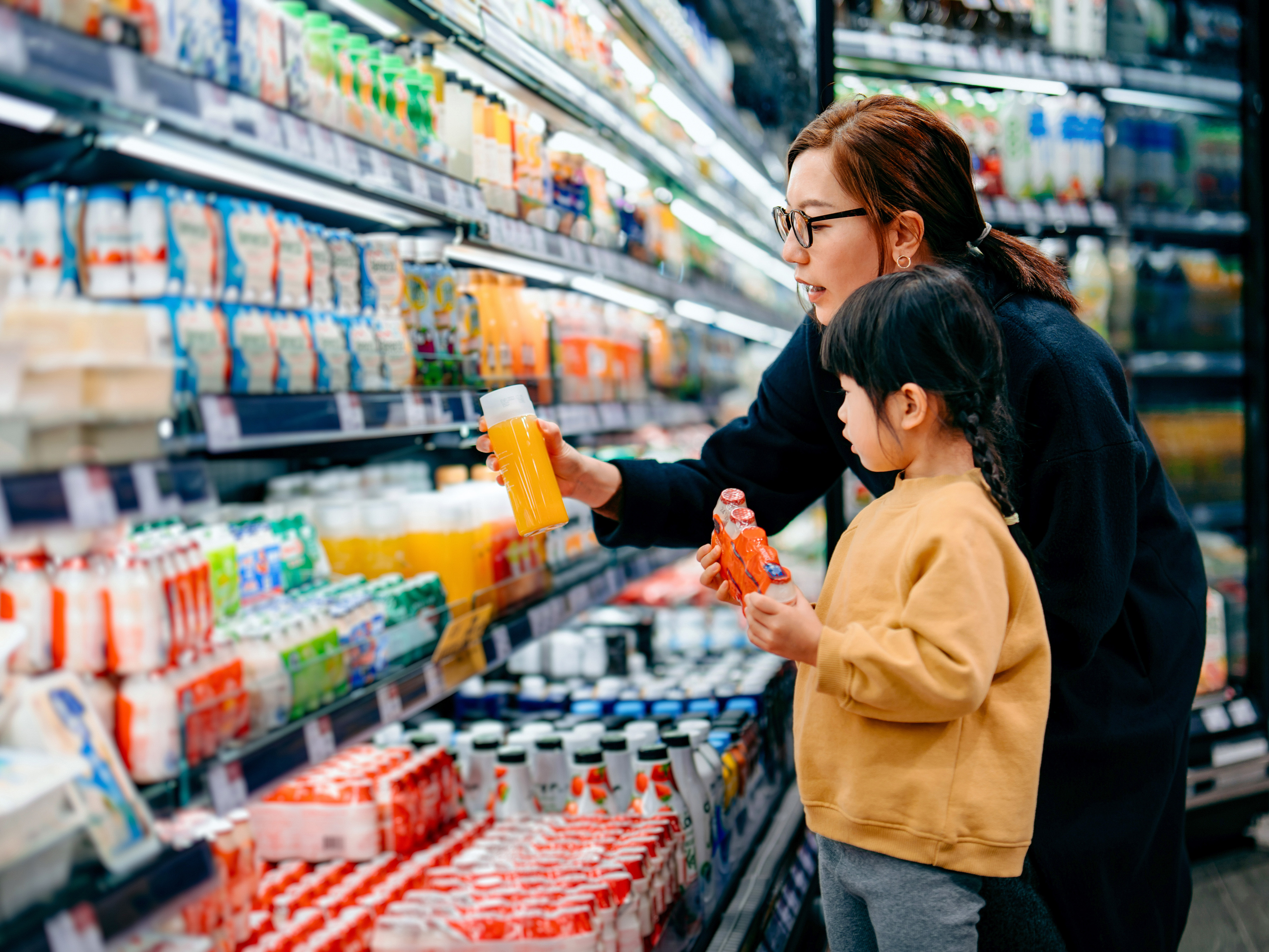 A parent and a child are shopping for beverages in front of a refrigerated section in a grocery store.