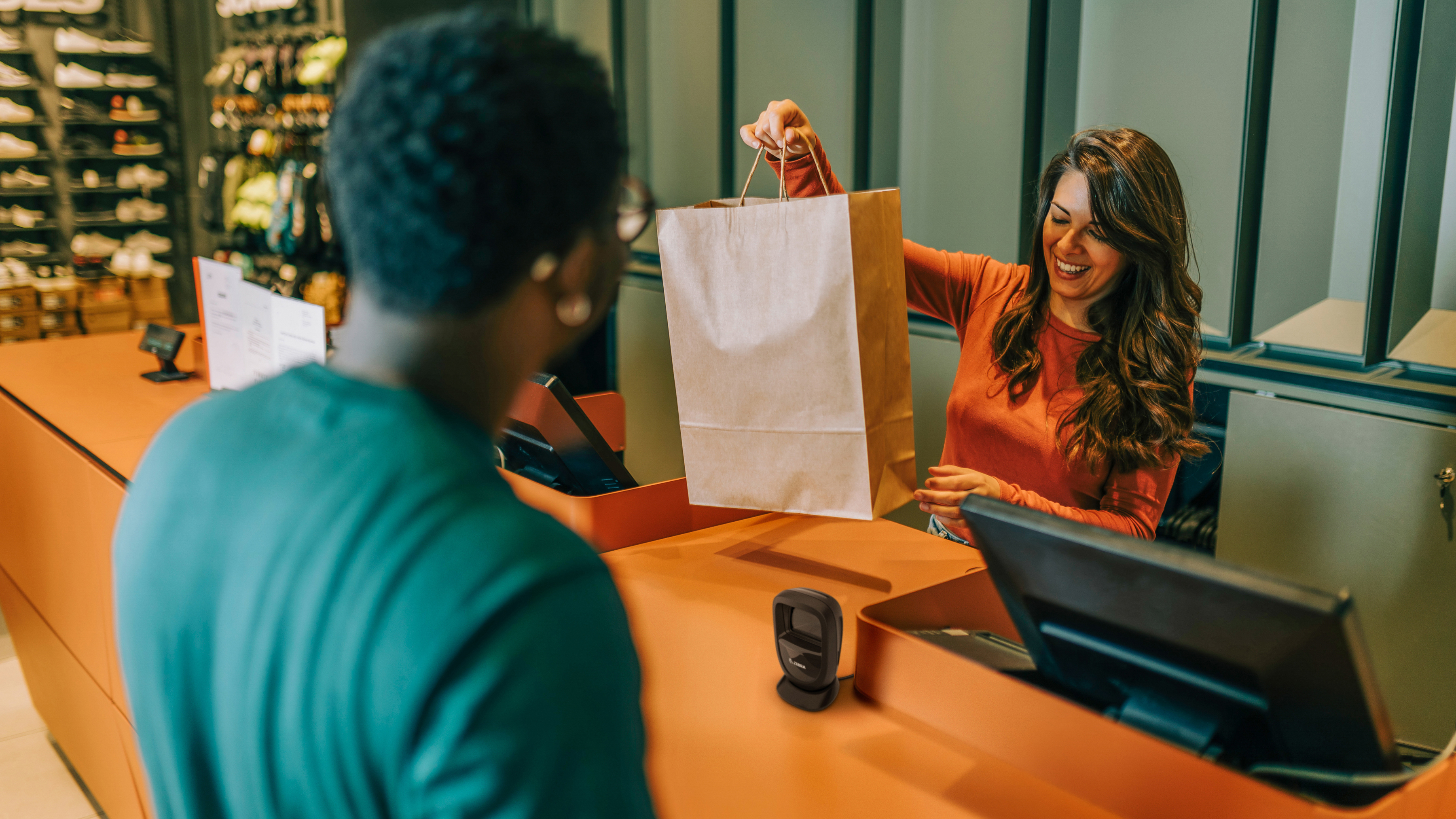 An employee handing a shopper their purchase at the checkout of a shoe store.