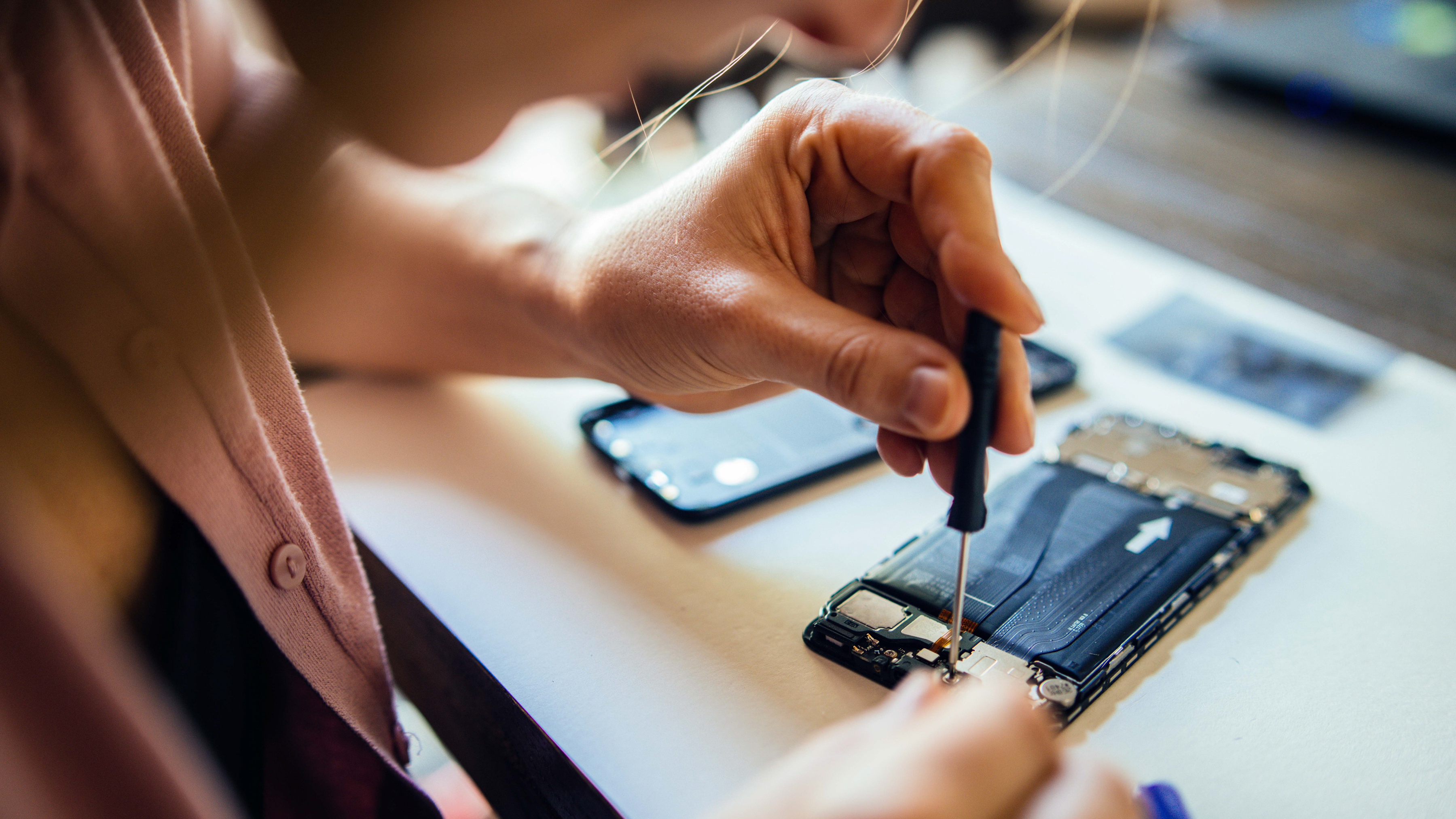 A person is using a screwdriver to repair the internal components of a mobile computer.