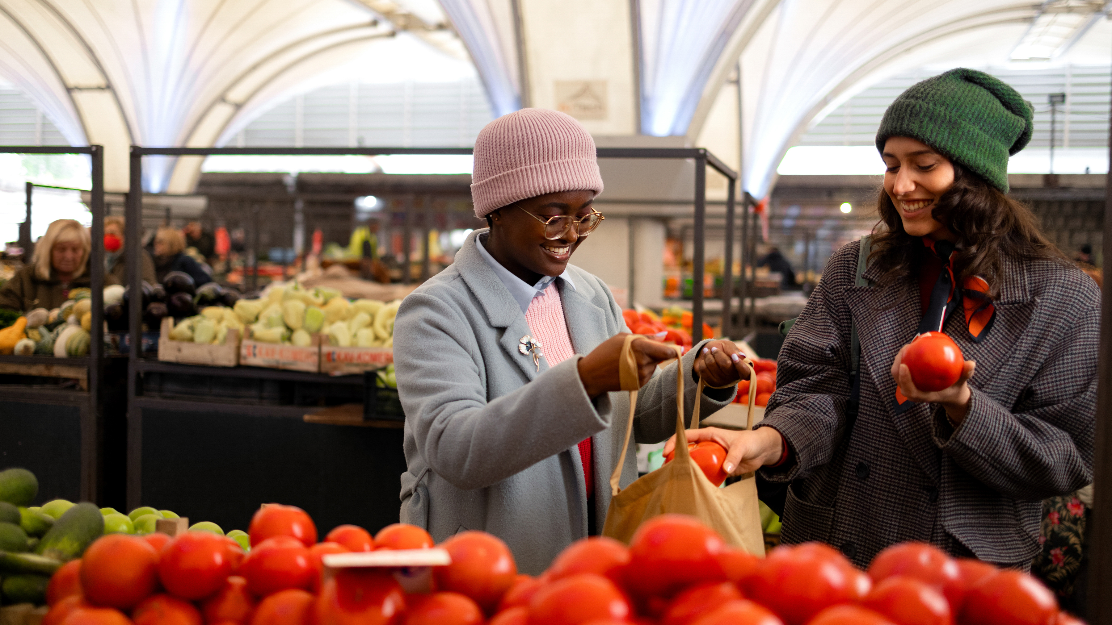 Two shoppers selecting tomatoes inside a grocery store produce department.