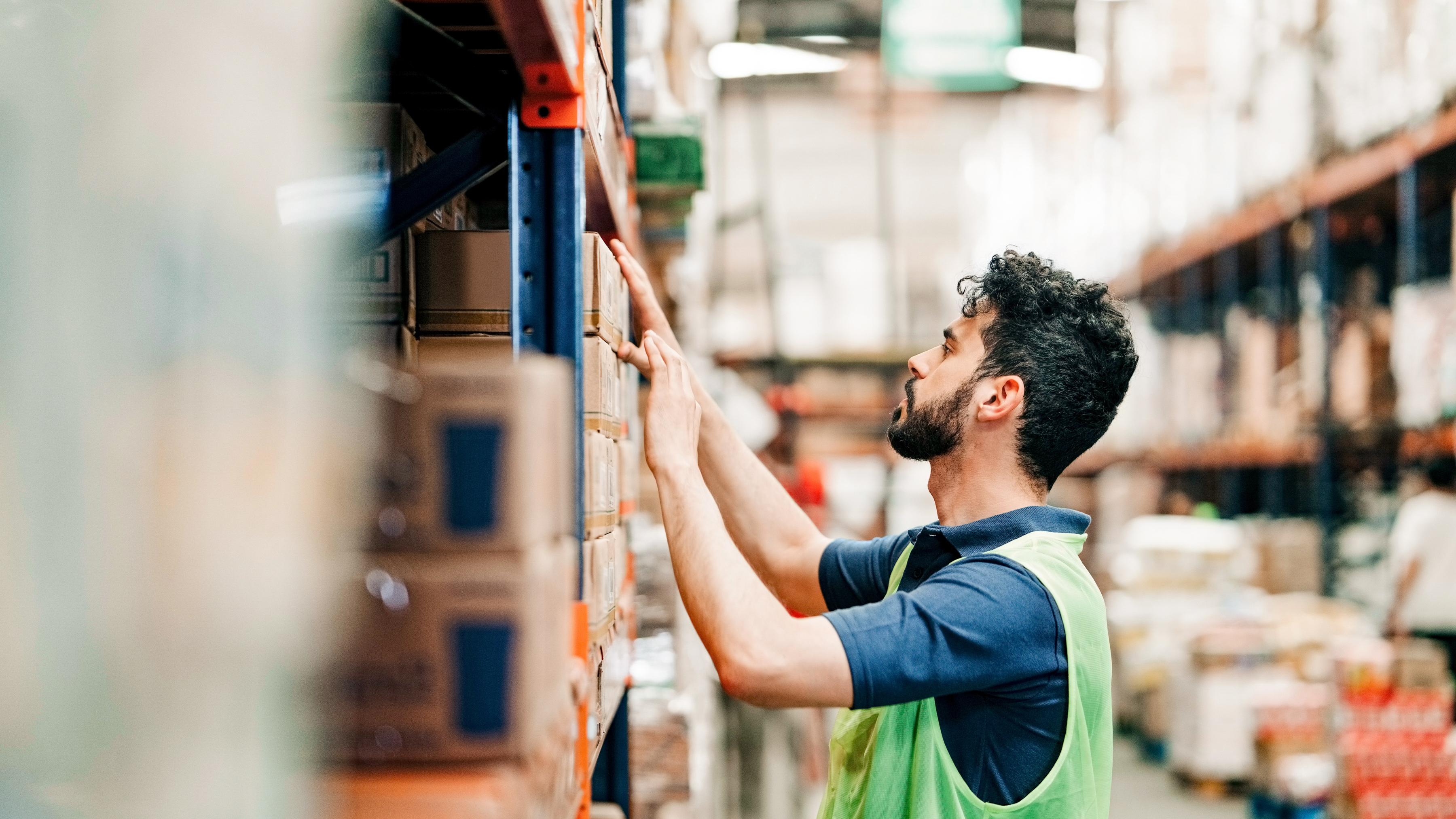 A worker is checking inventory on a shelf in a warehouse.