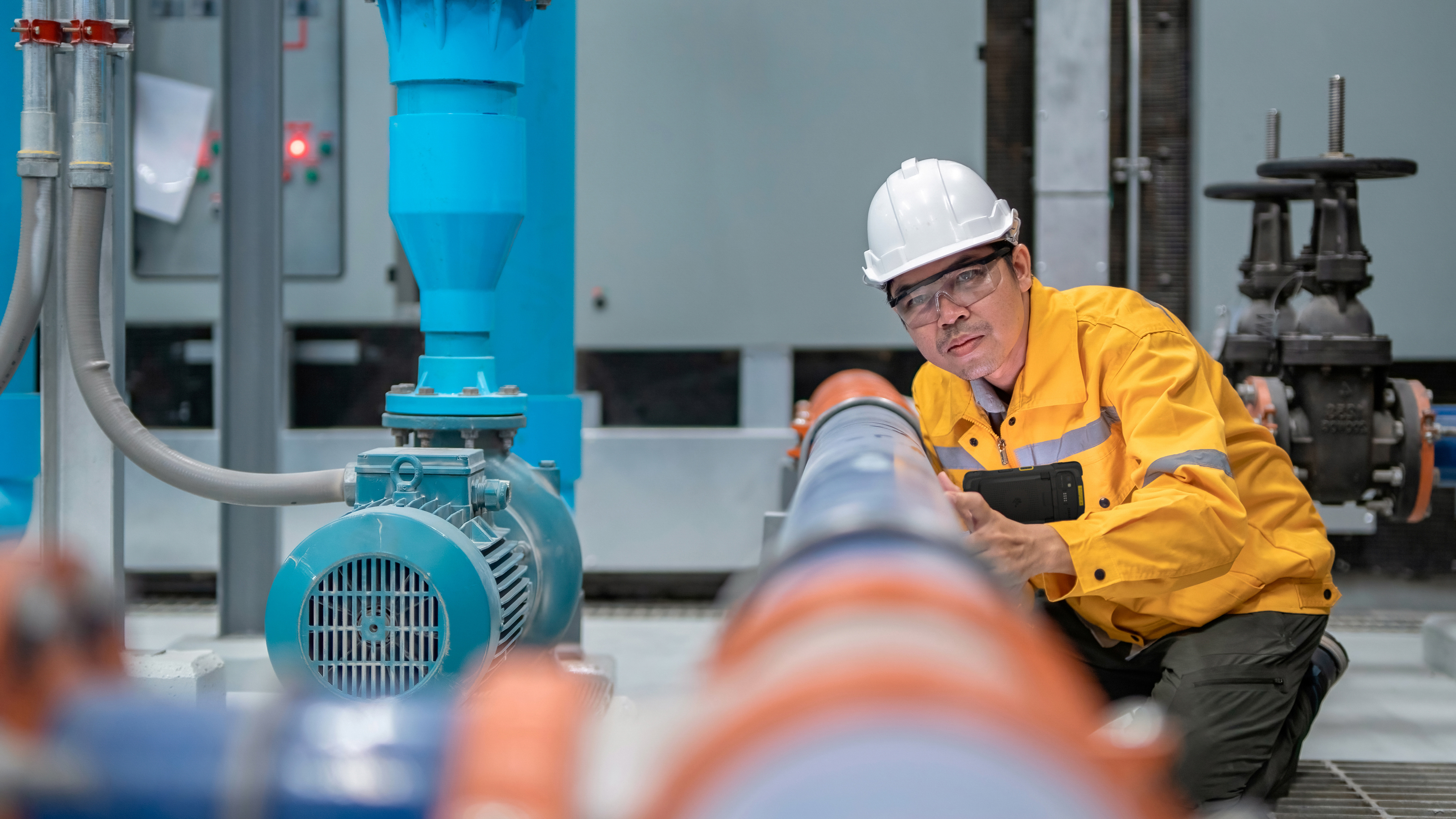 An engineer using a handheld mobile computer to inspect a water pump.