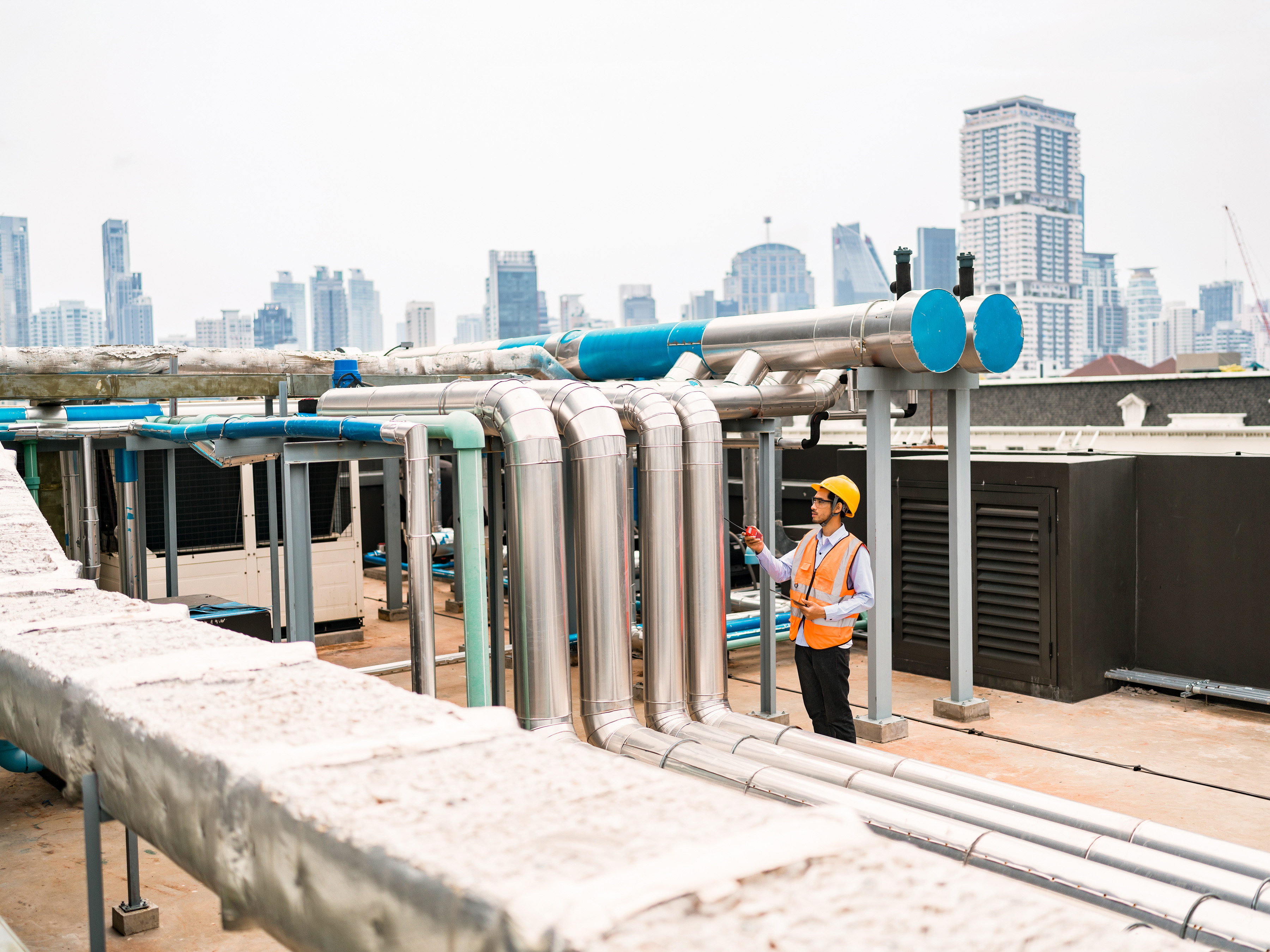Engineer inspecting industrial piping on the roof of a city building.