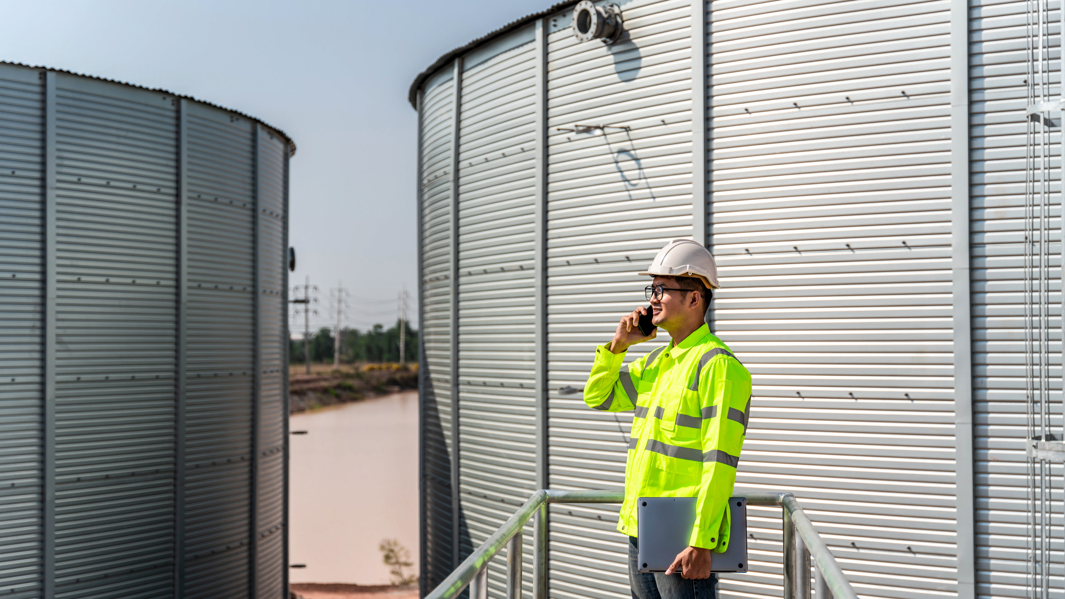 An industrial worker on a phone call using a mobile computer holding a laptop at a production site.