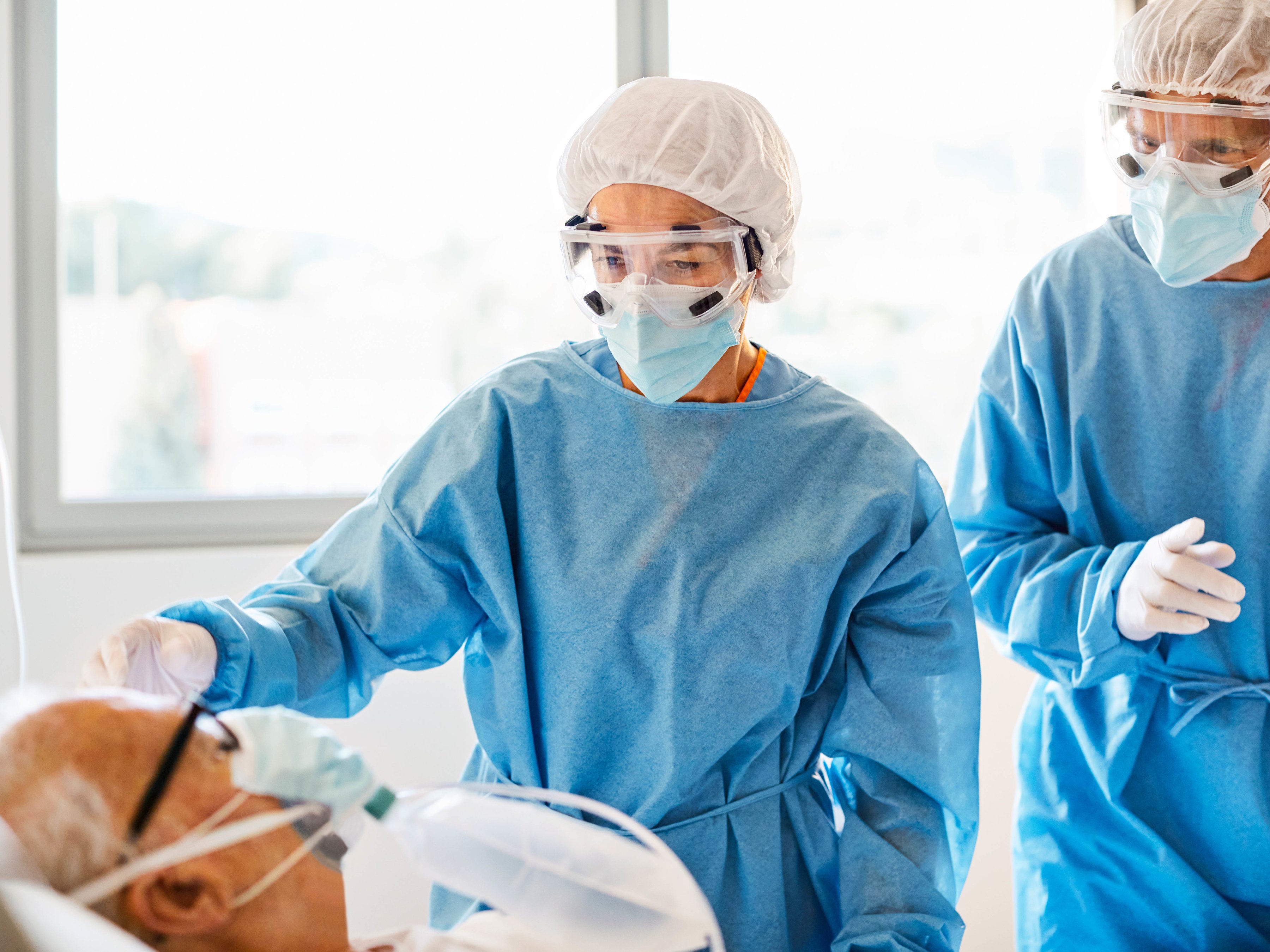 Two healthcare workers in full nursing scrubs providing care for a patient.