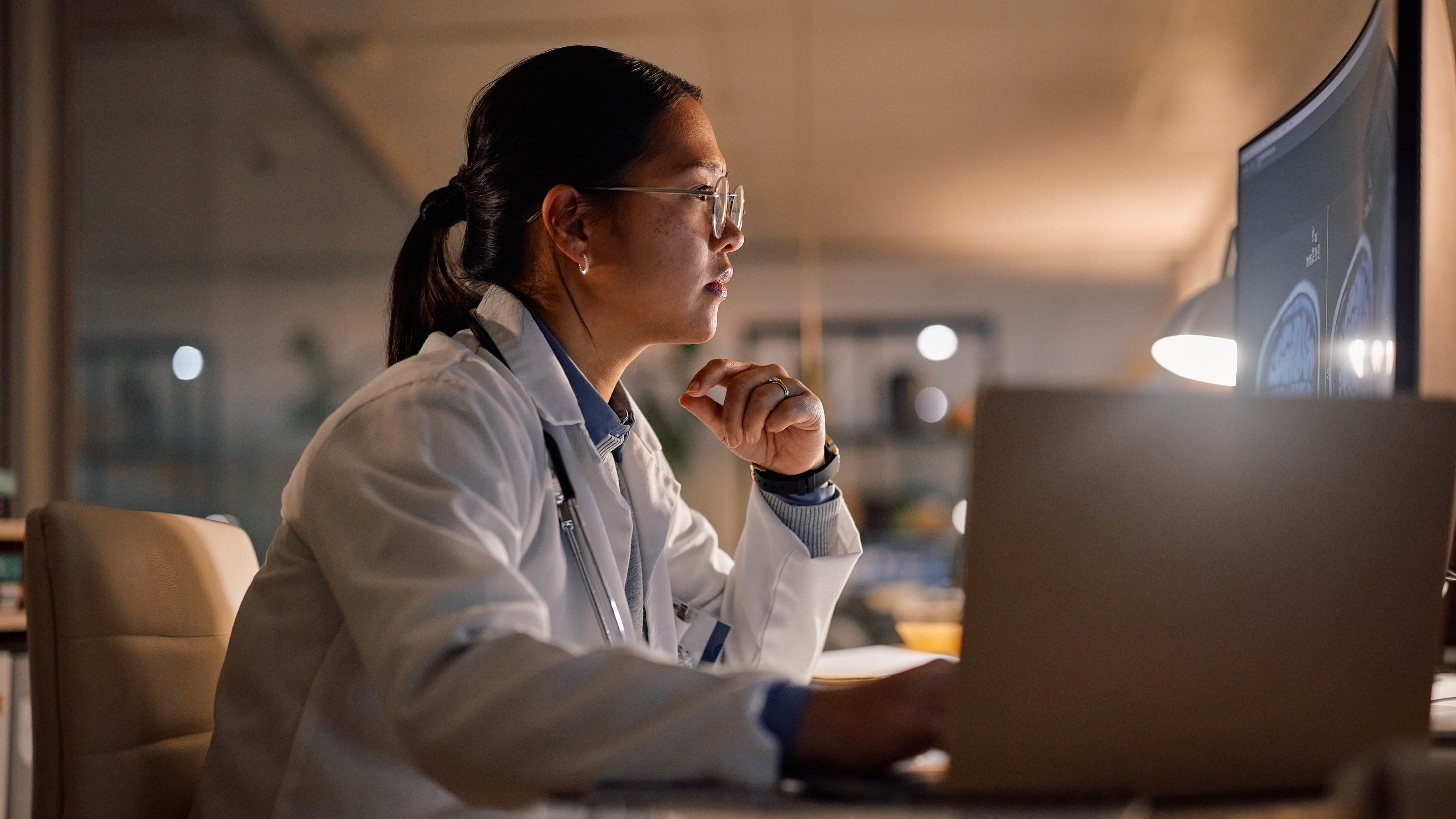 A medical professional reviewing x-rays on a laptop and desktop monitor.