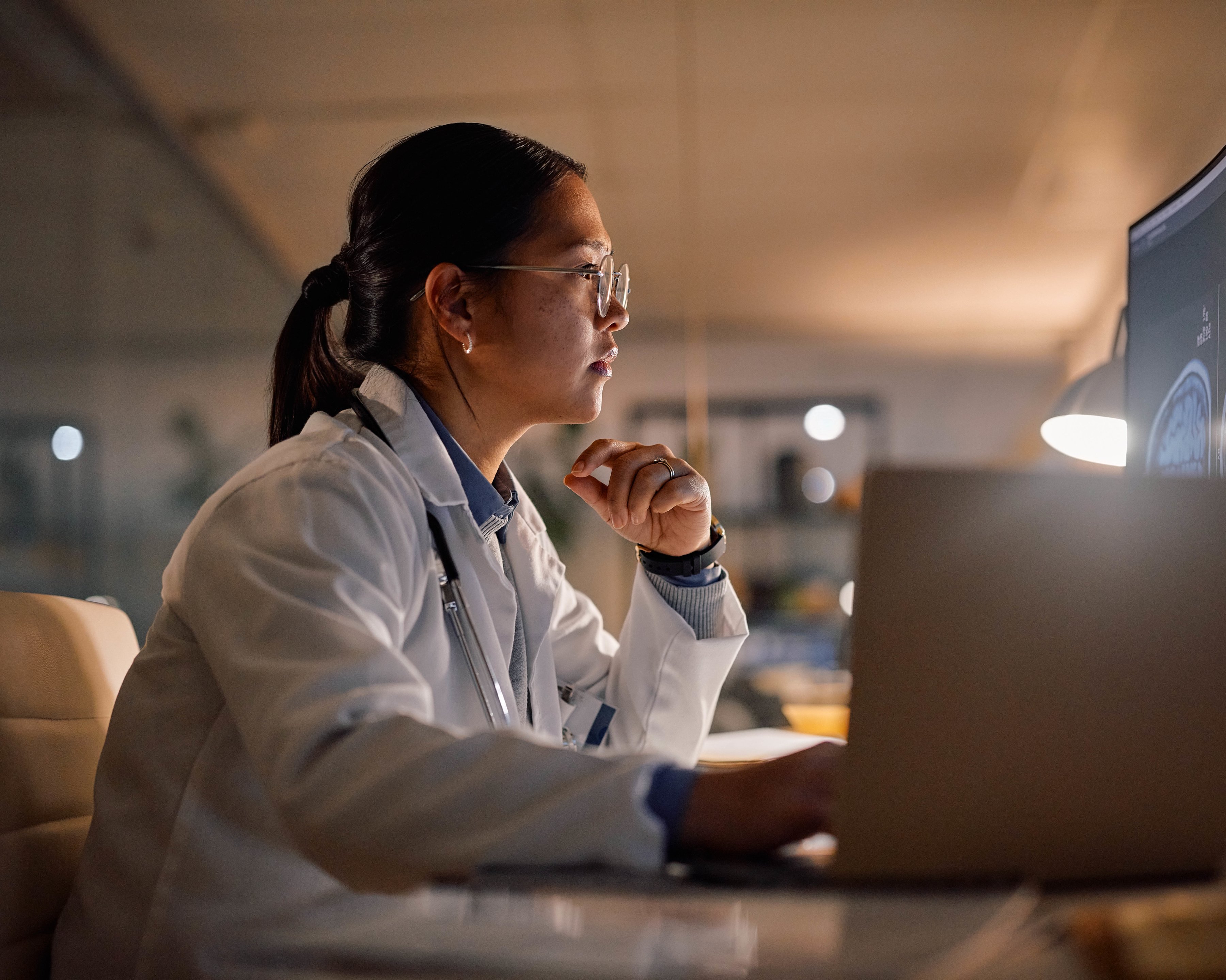 A medical professional reviewing x-rays on a laptop and desktop monitor.