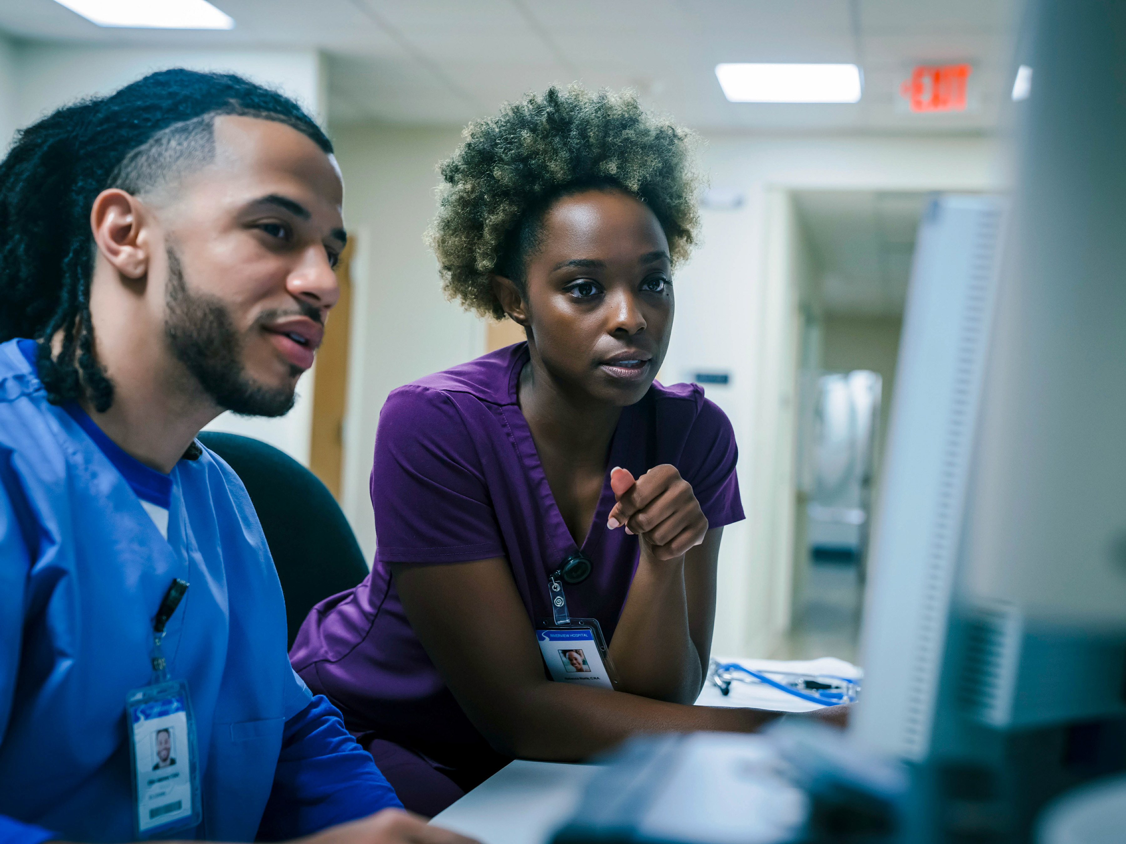 Two medical professionals looking at a desktop computer inside of a hospital.