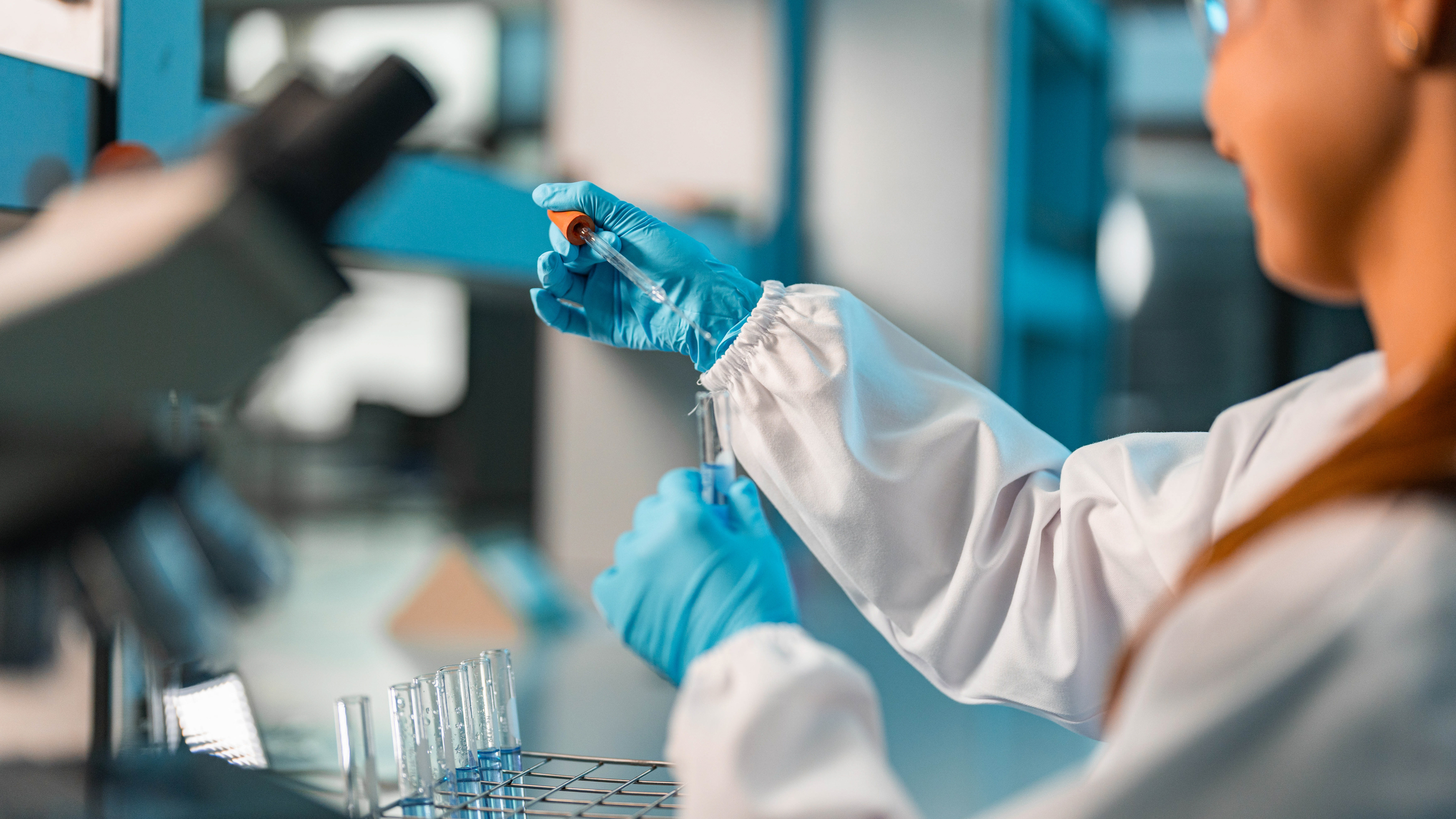 A laboratory worker in goggles working with a vial.