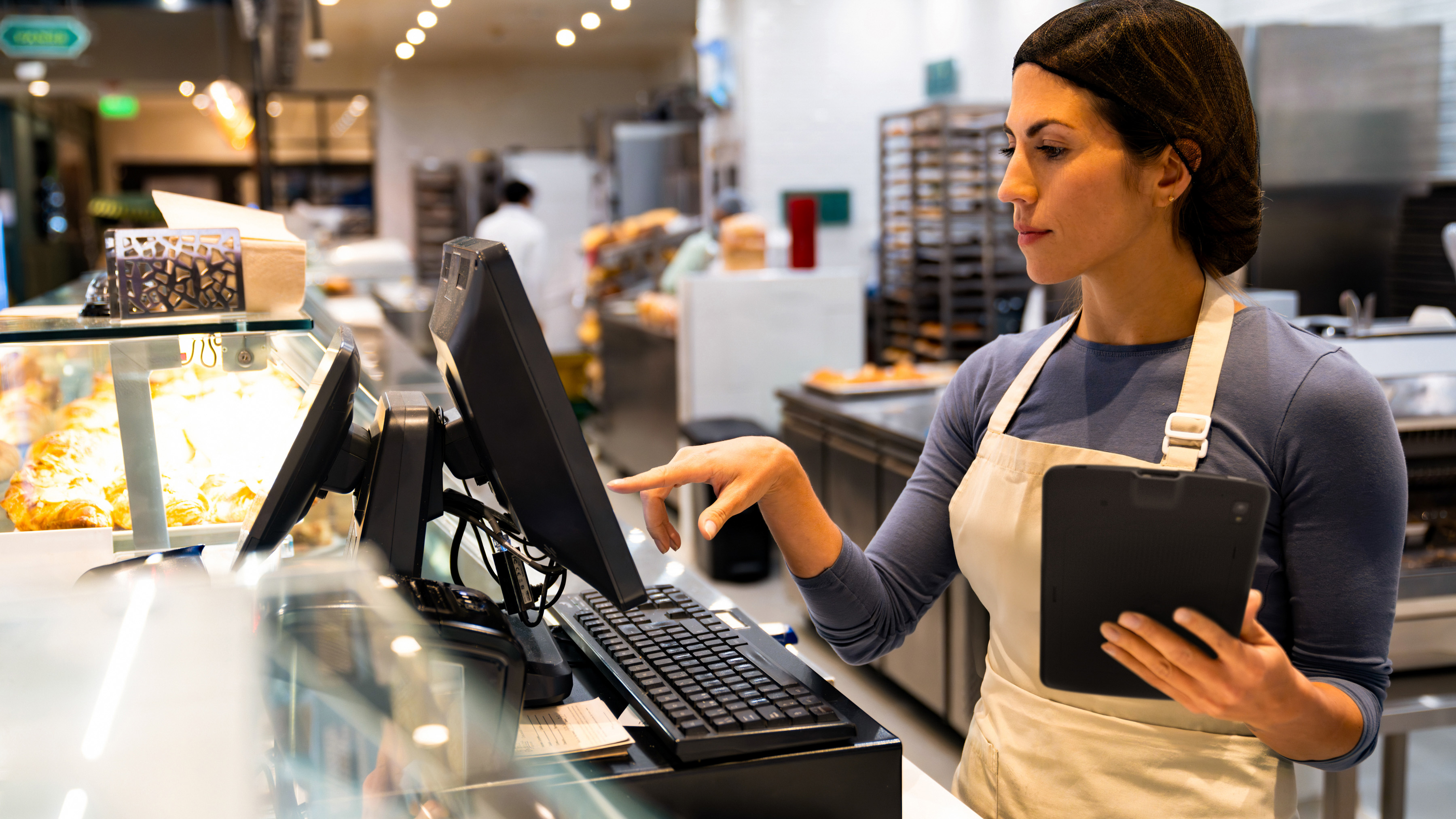 A bakery employee holding a Zebra tablet and using an interactive kiosk  for checkout at the cash register.