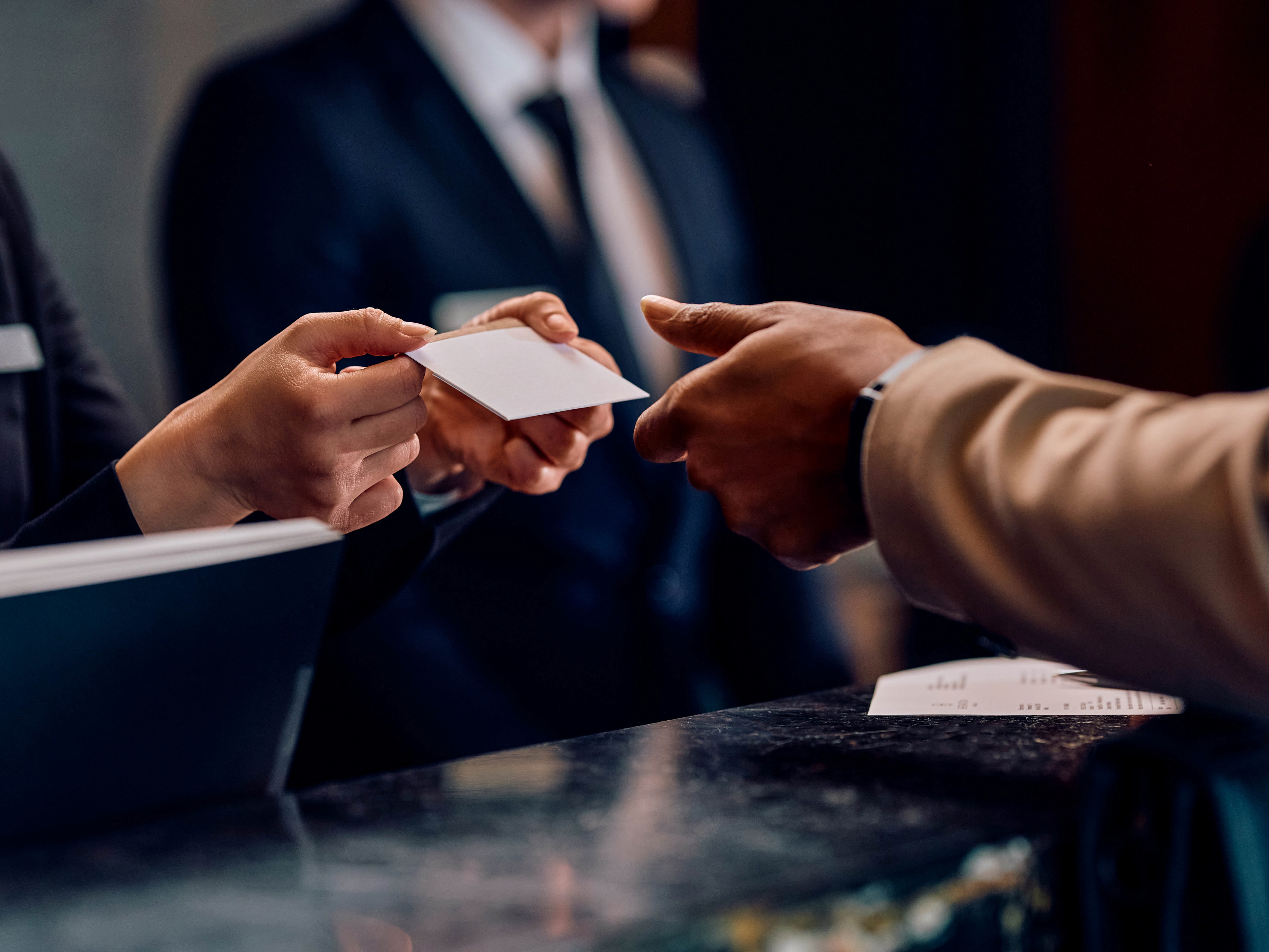 A front desk attendant providing a room key to a customer inside of a hotel lobby.