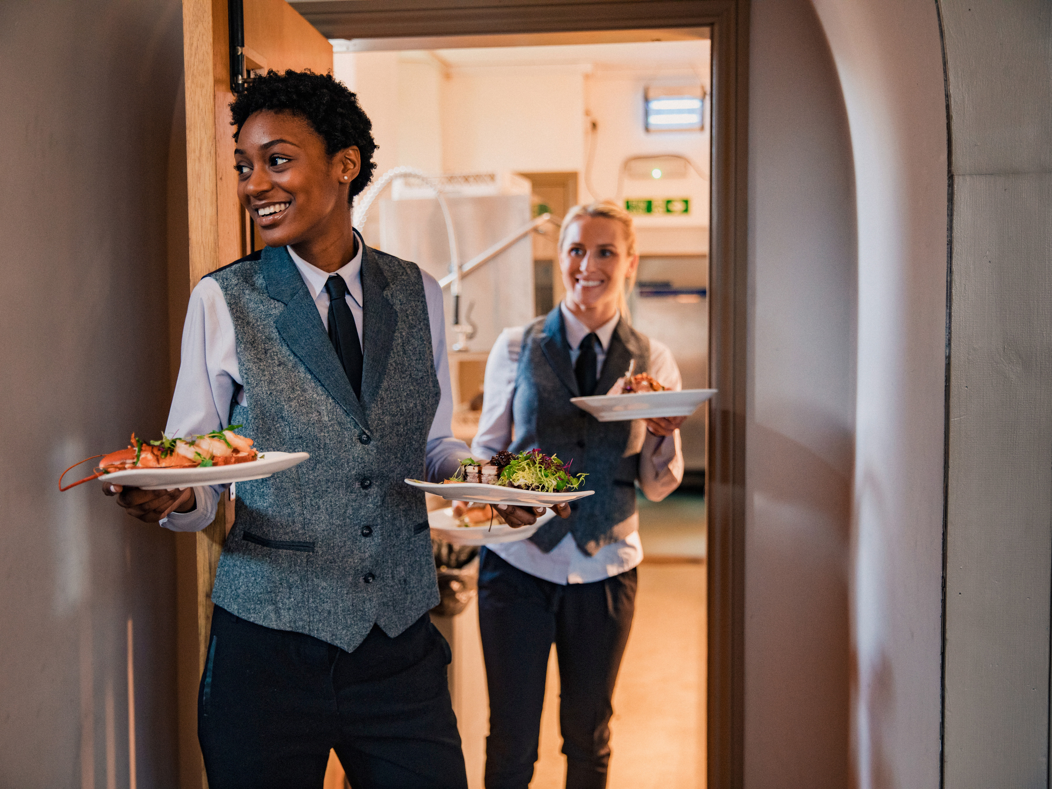Dining servers carrying food plates from a commercial kitchen.