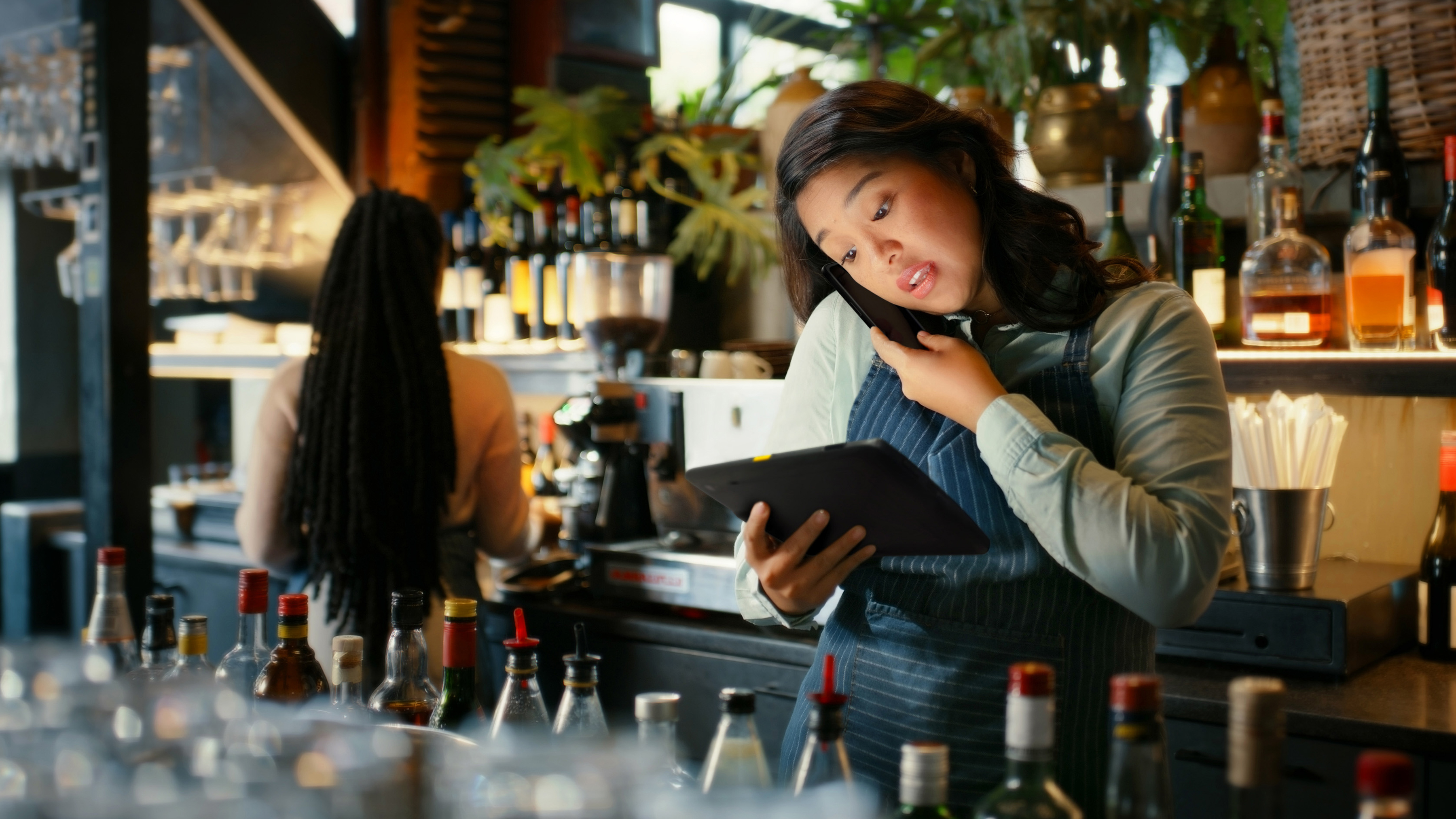 Hospitality worker using a Zebra tablet and speaking on a mobile computer behind a bar.