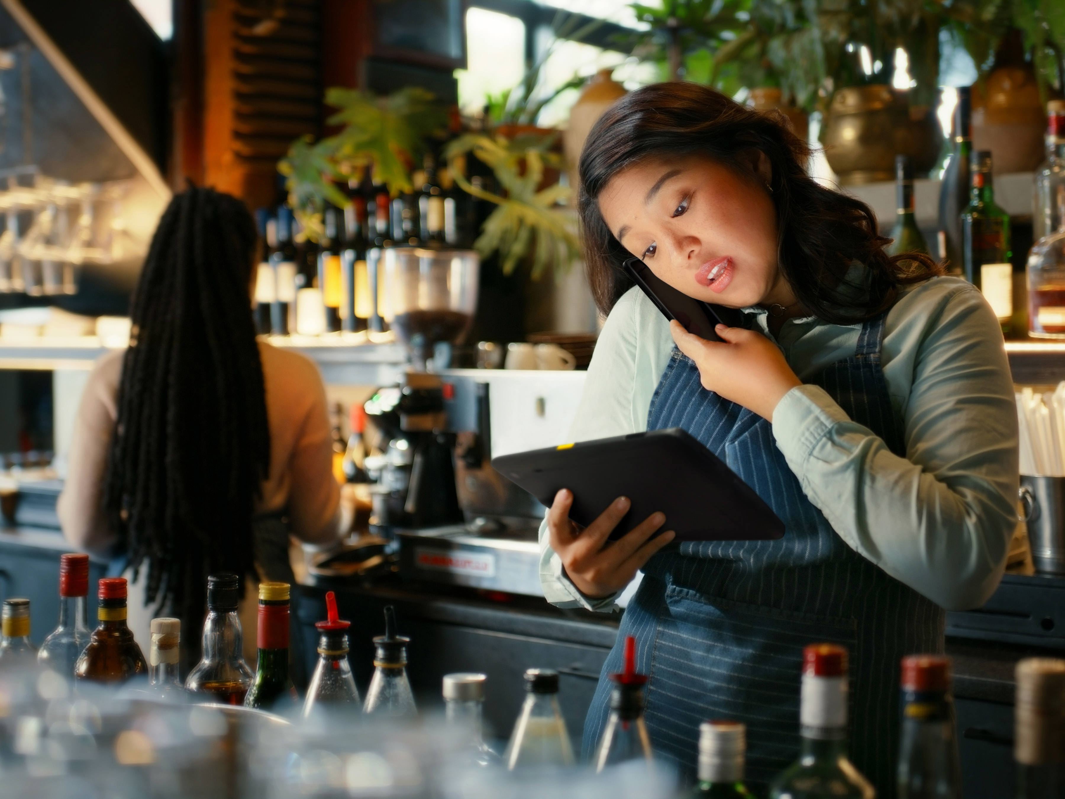 Hospitality worker using a Zebra tablet and speaking on a mobile computer behind a bar.