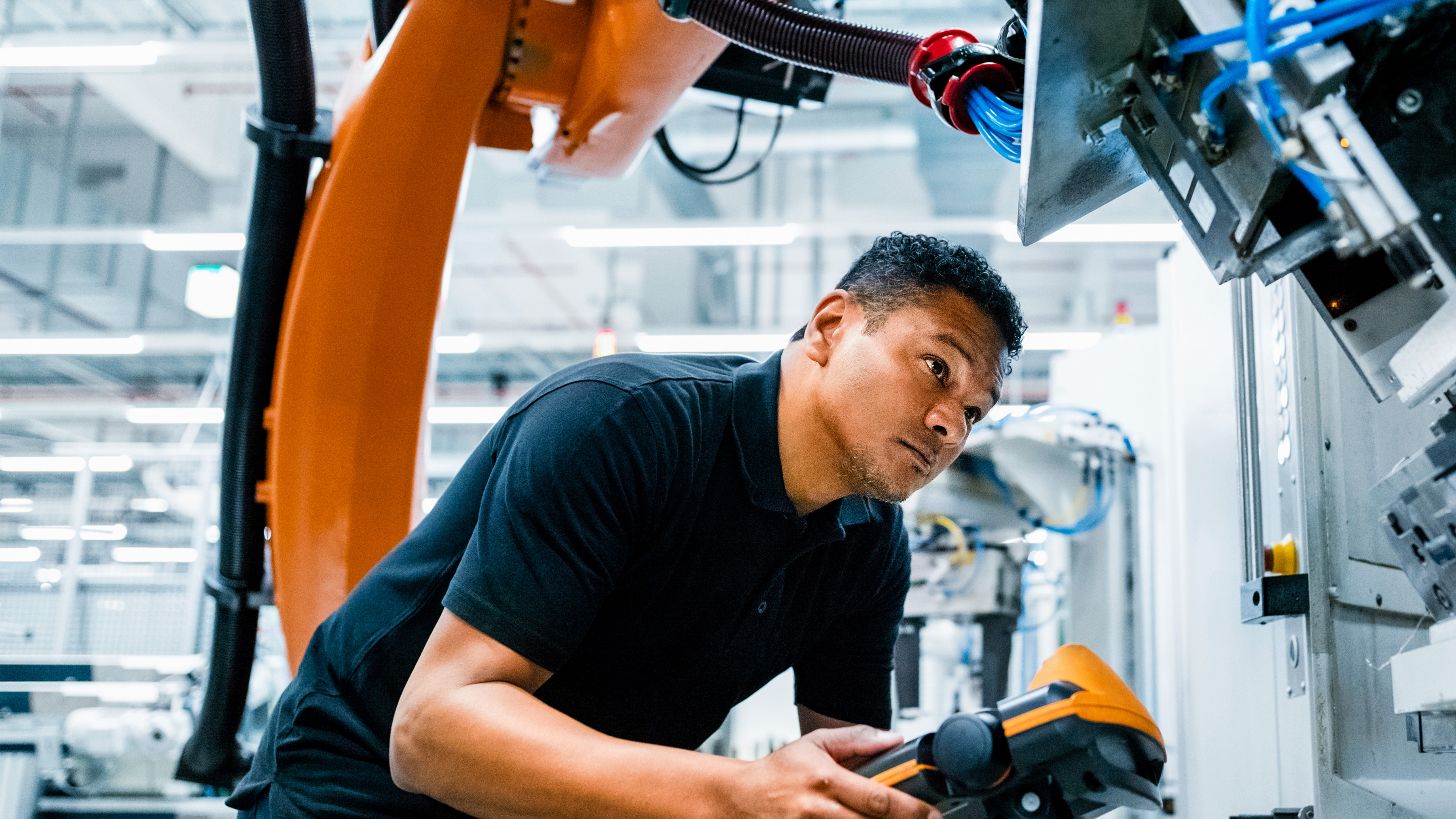 An engineer operates a robotic arm in an industrial setting using a handheld control device.
