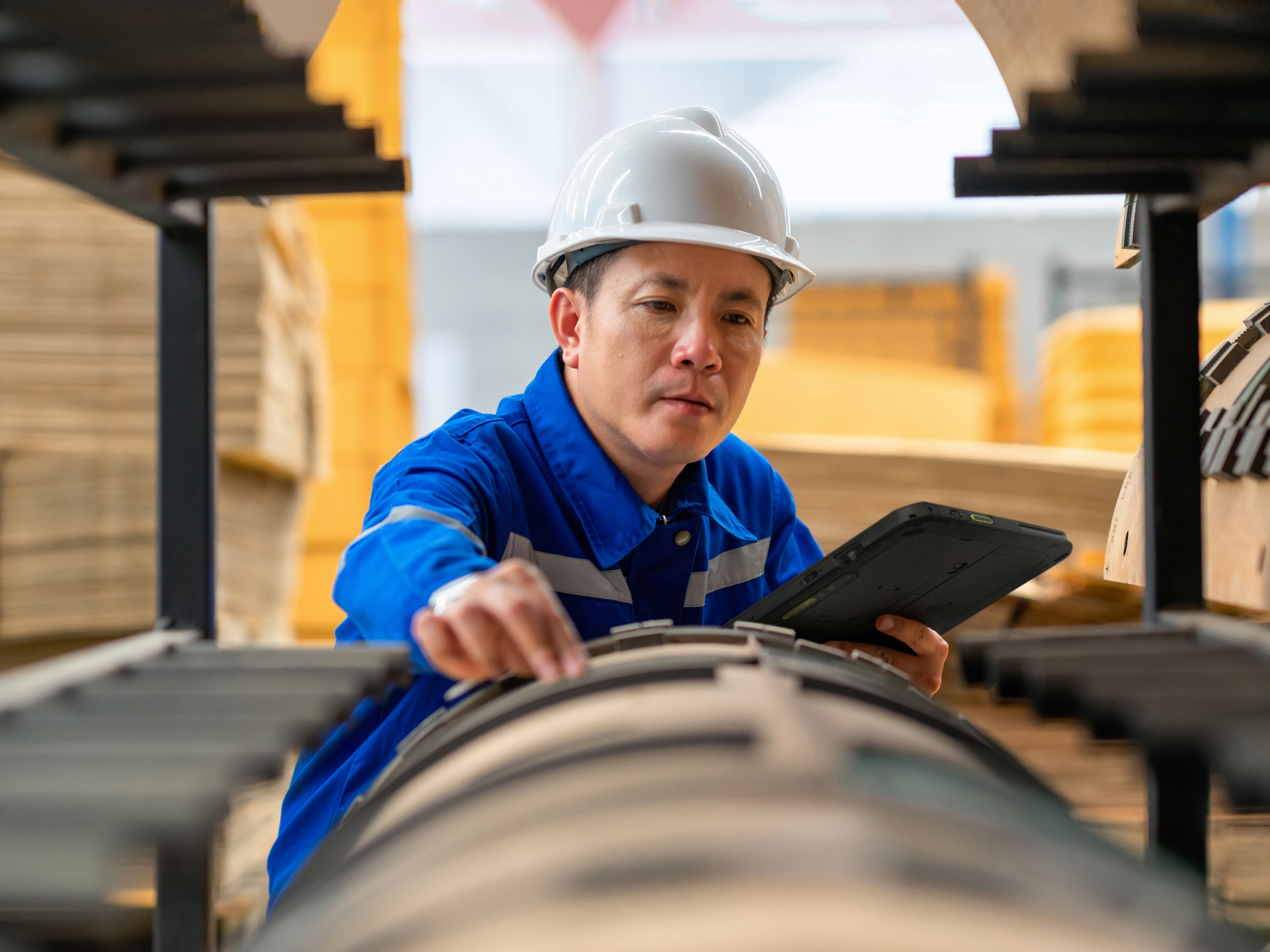 An engineer reviewing a tablet during a quality control inspection inside of a manufacturing plant.