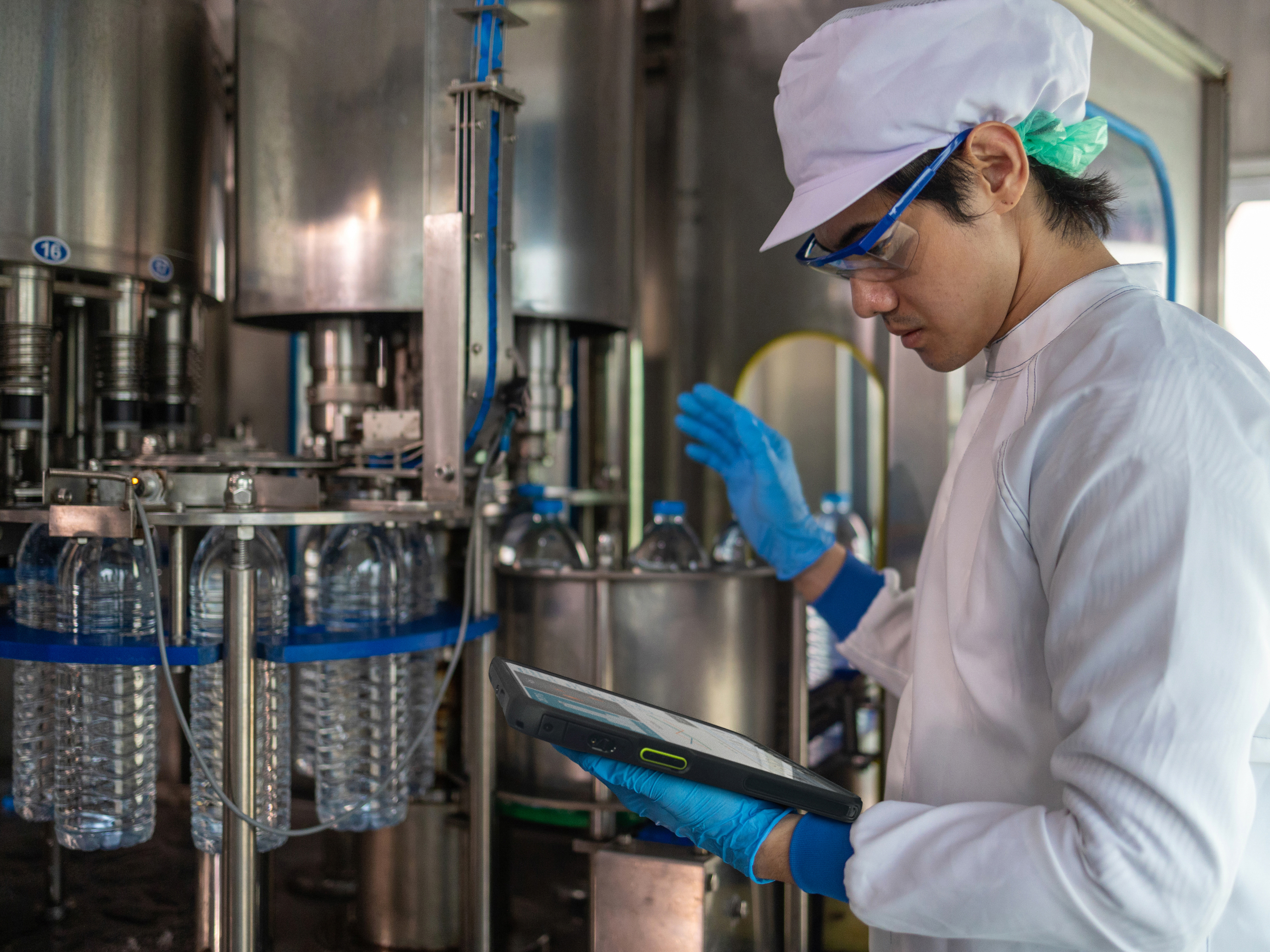 An engineer reviewing a tablet inside of a water bottle manufacturing facility.