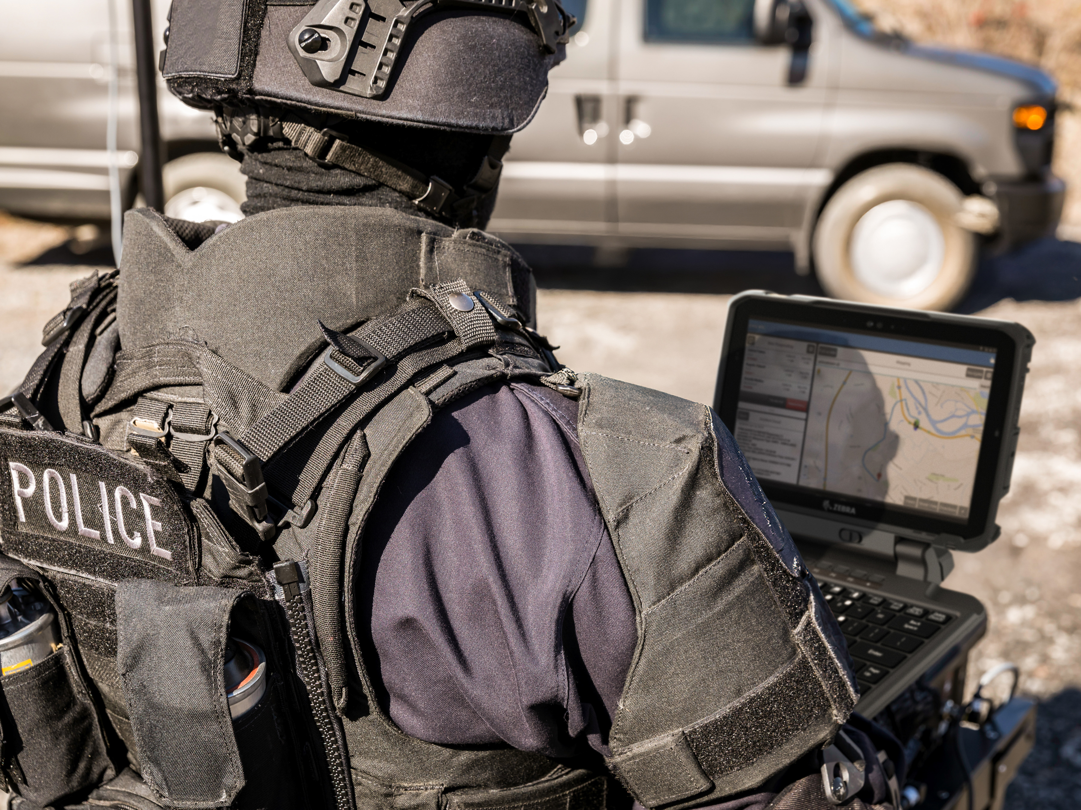 A tactical police officer using a Zebra rugged handheld tablet during a field operation.