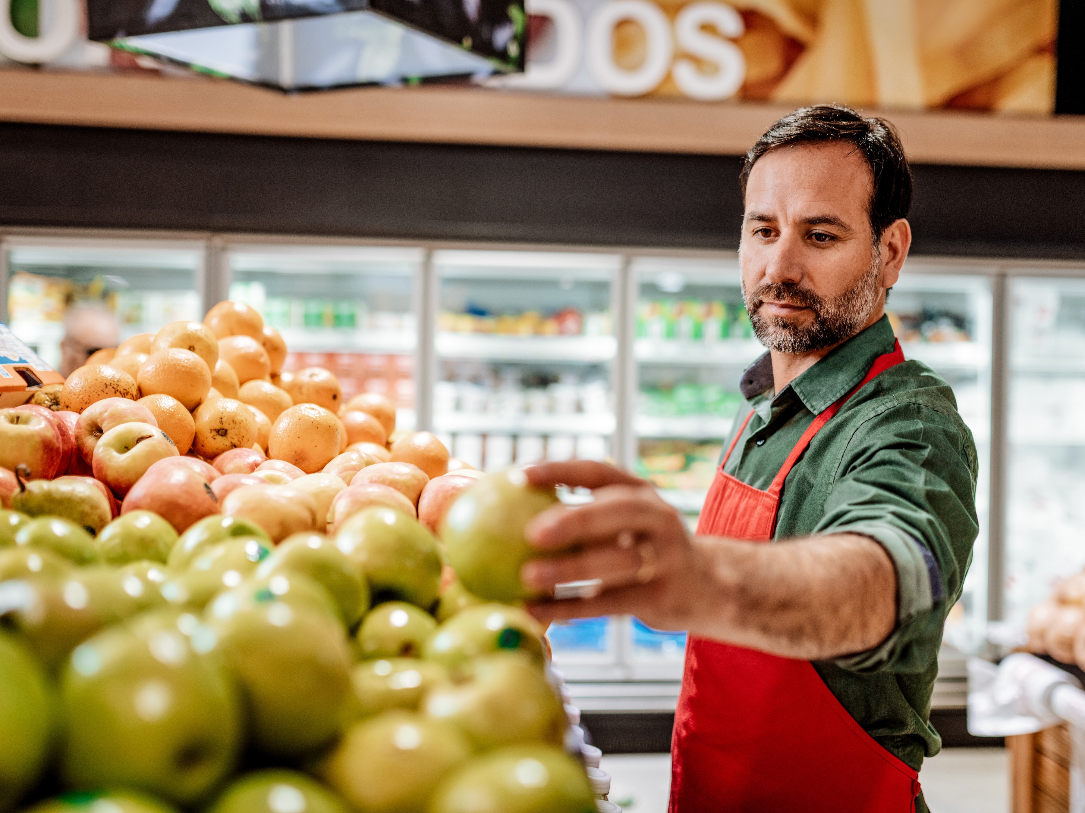 A grocery store worker is organizing green apples in a fruit display.