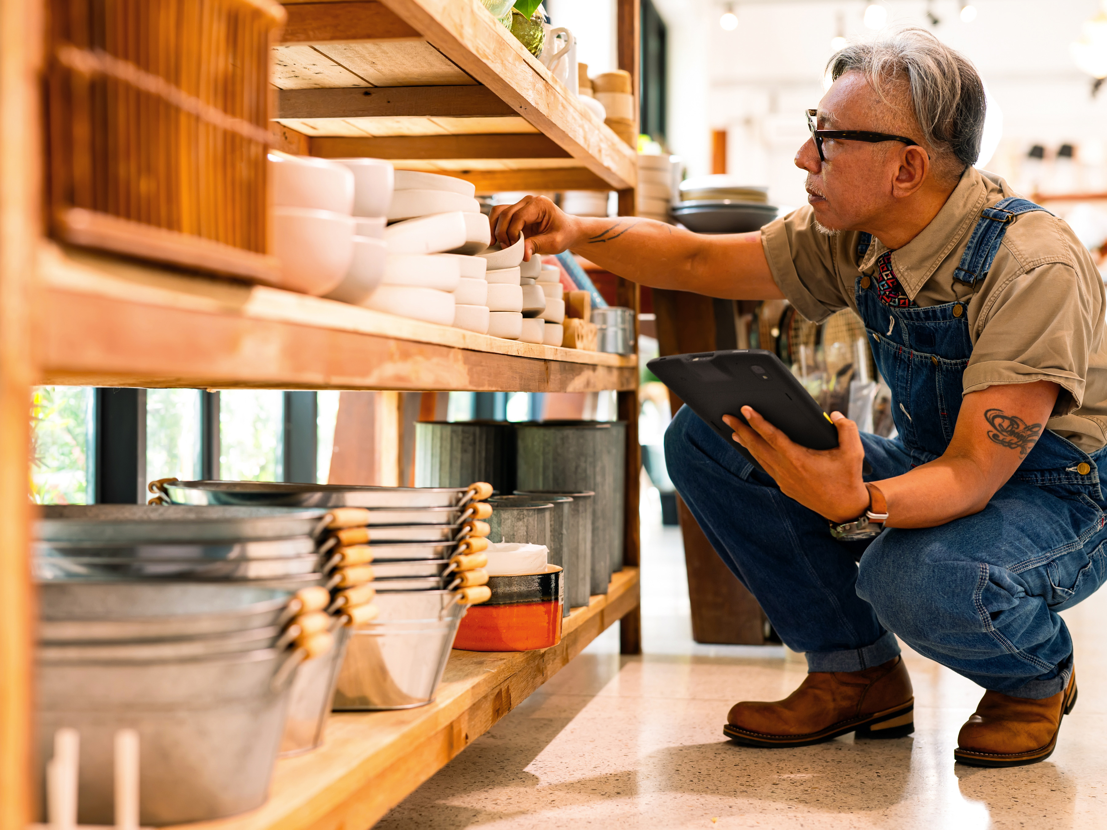 A retail employee checking shelf inventory with a tablet inside a store's back-of-house.
