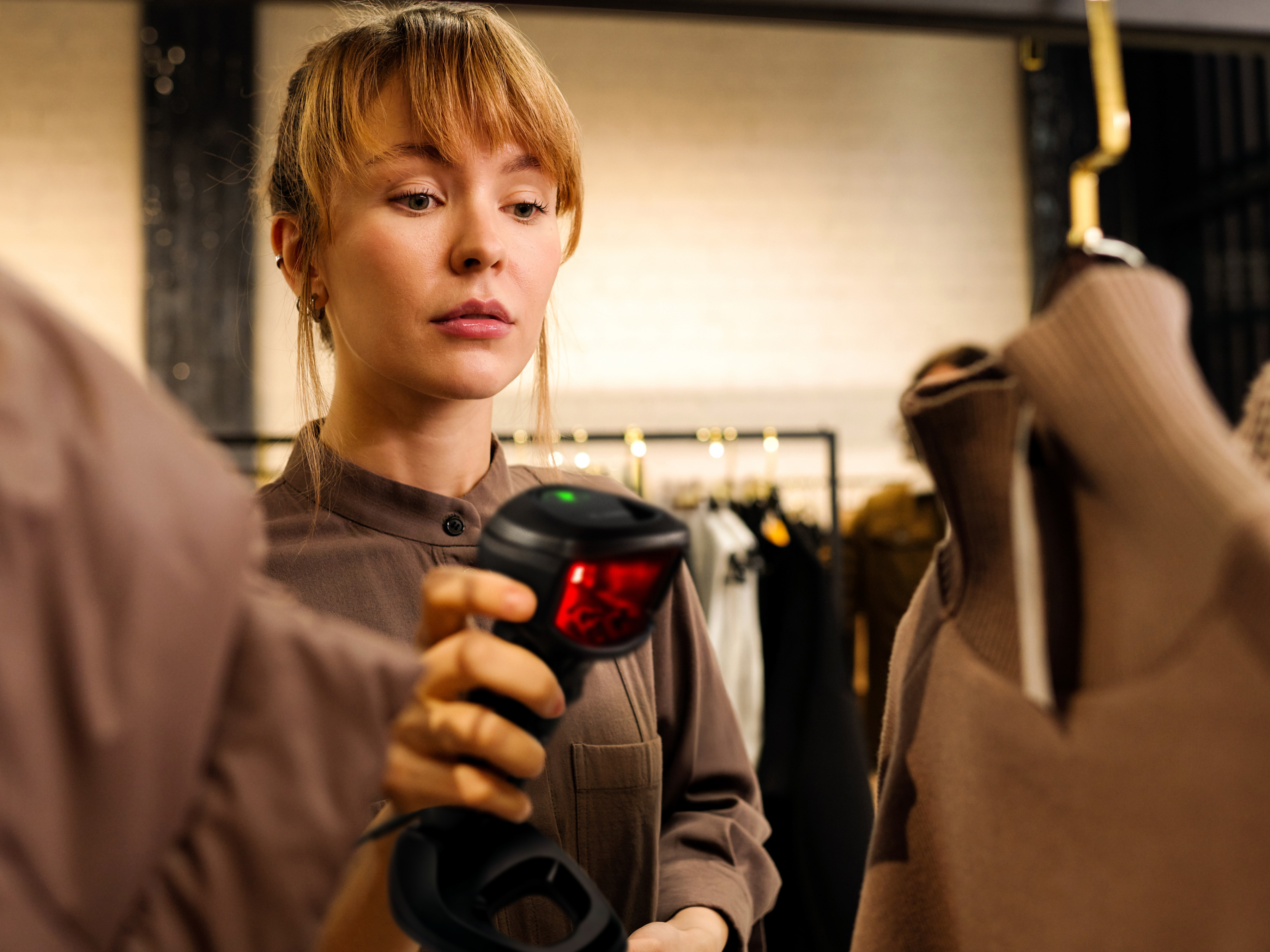 A front-of-house employee using a handheld barcode scanner to scan a price tag on a shirt inside of a clothing store.