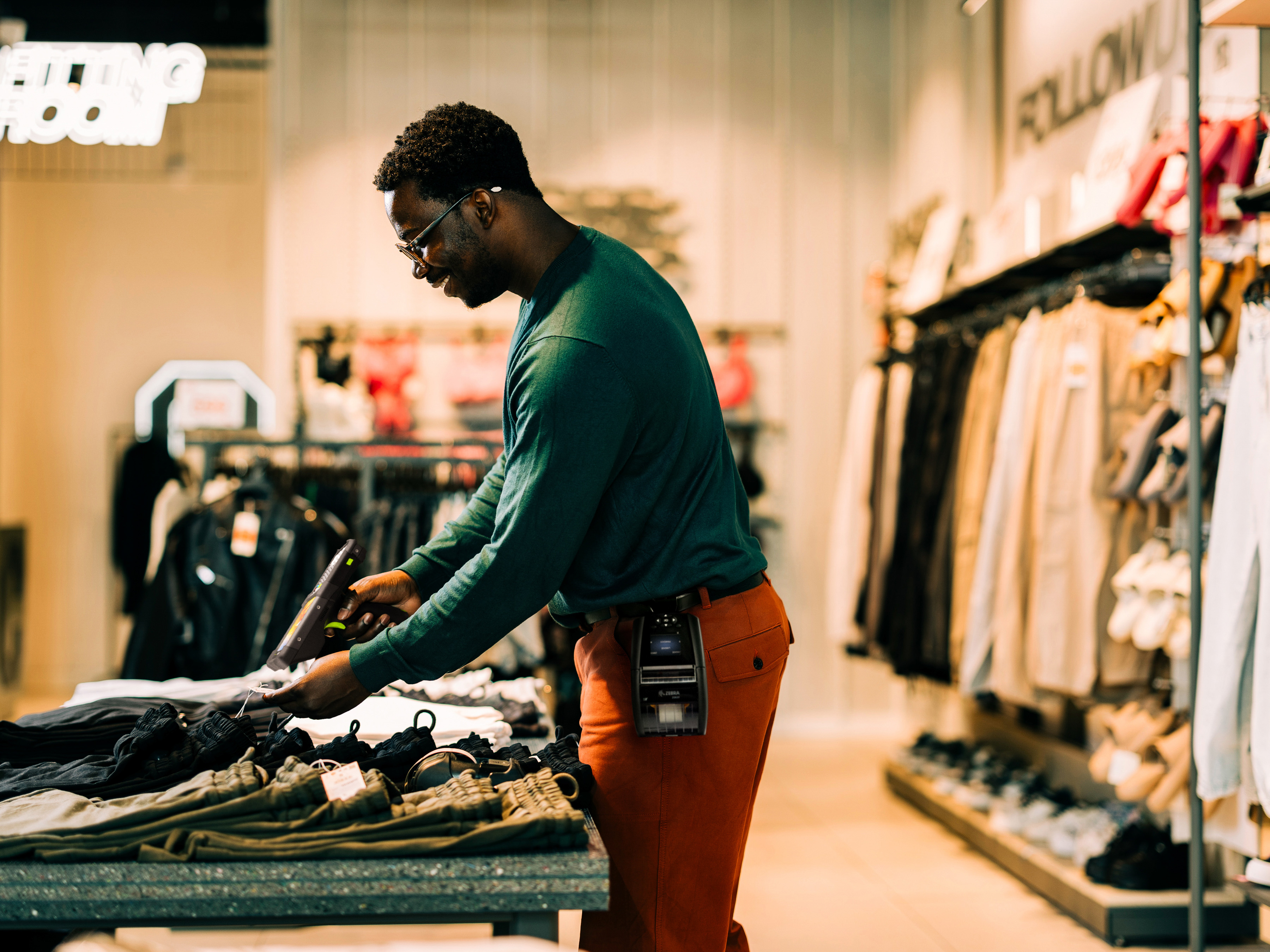 A front-of-house employee using a handheld barcode scanner to scan clothing inside of a clothing store.