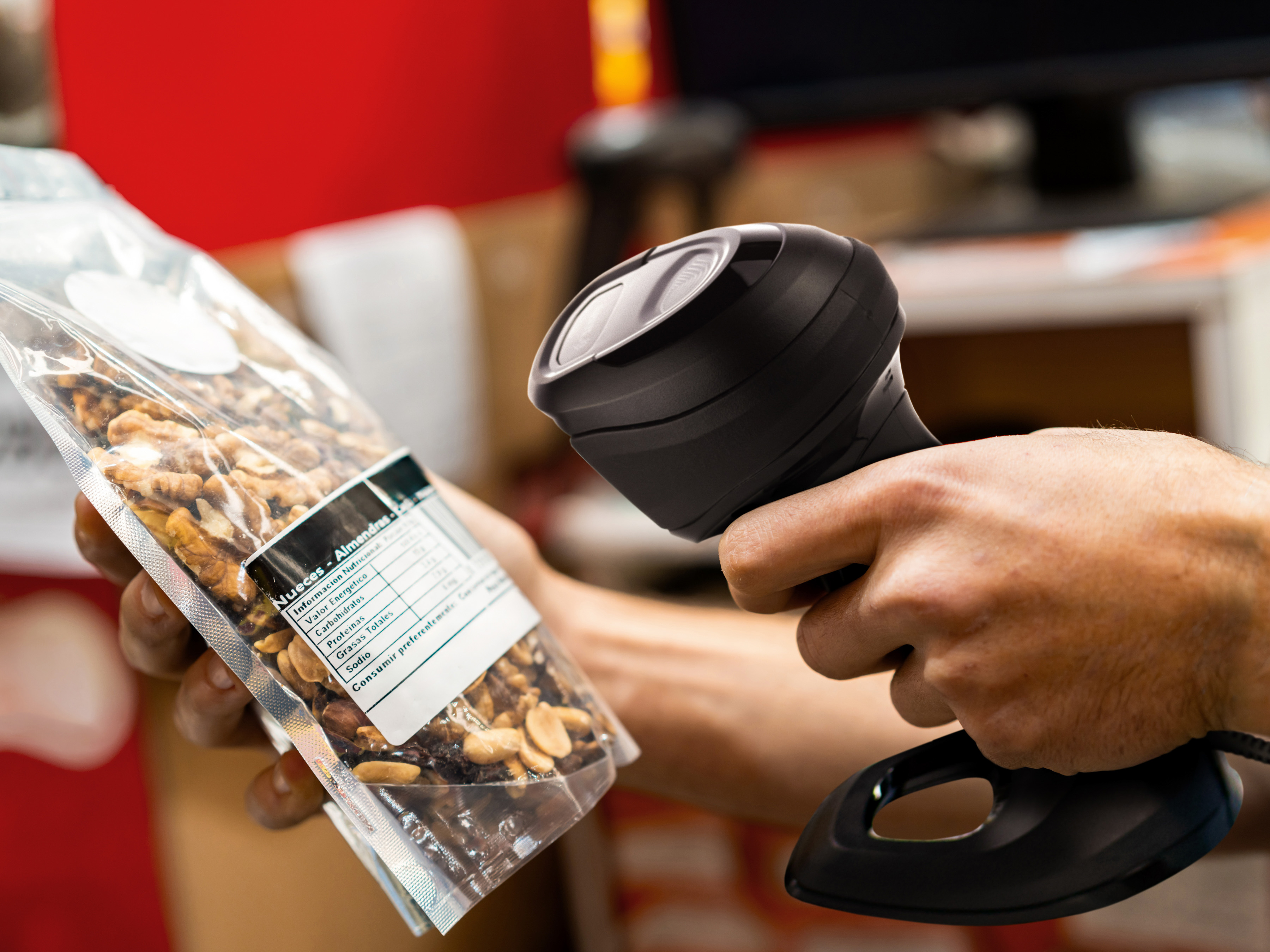 An employee using a handheld barcode scanner to scan a package of nuts inside of a grocery store.