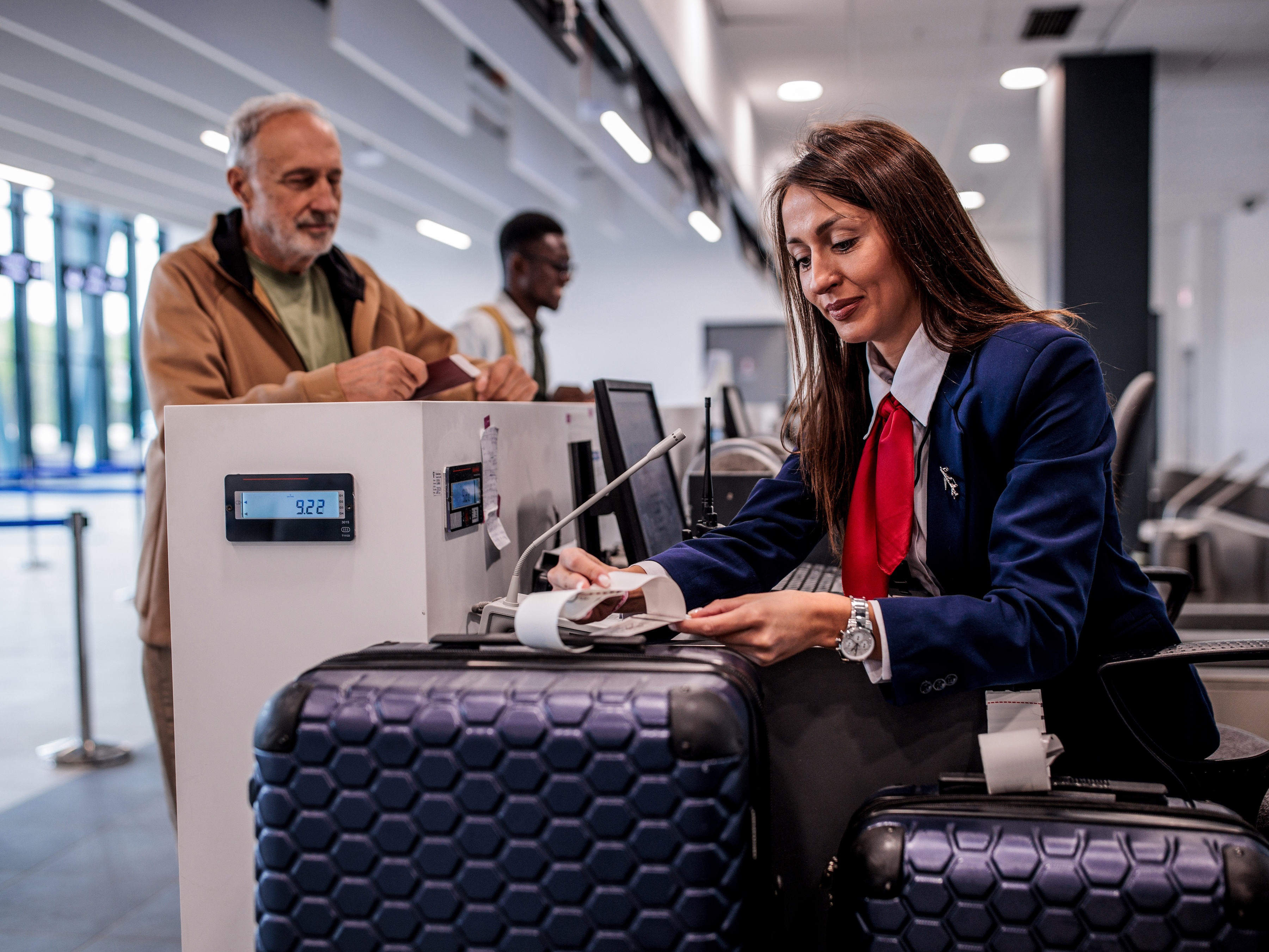 An airport worker is tagging a traveler 's luggage at an check-in counter.