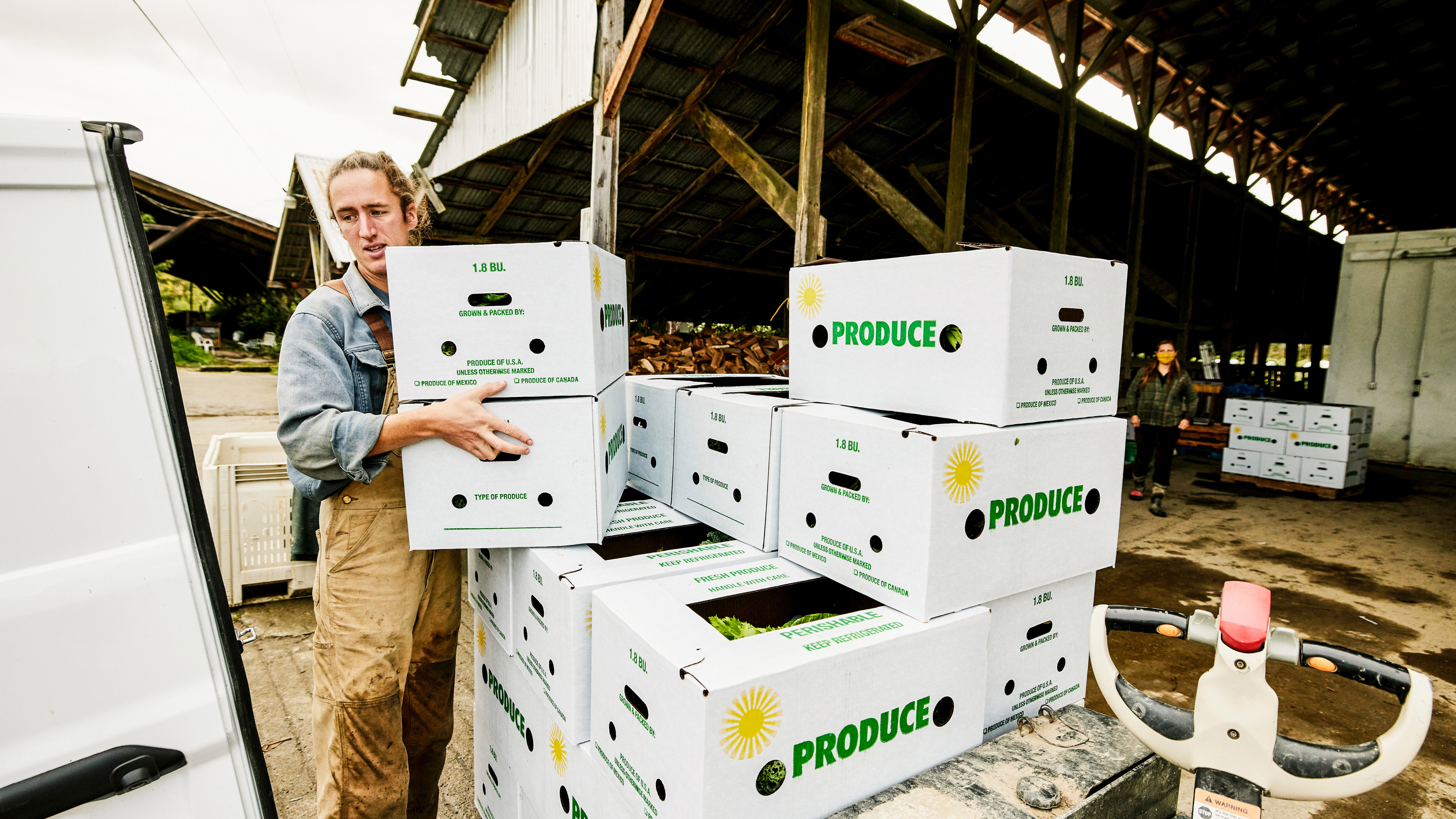 A worker is loading white boxes of produce into a vehicle near a warehouse.
